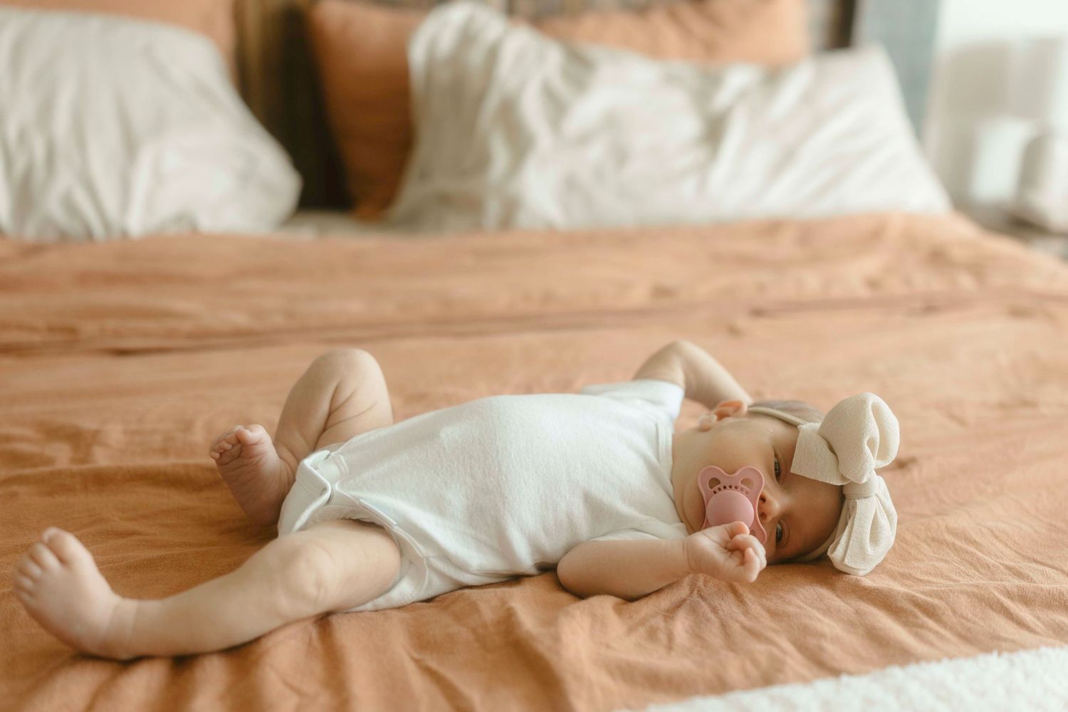 A newborn baby stretching on a bed.