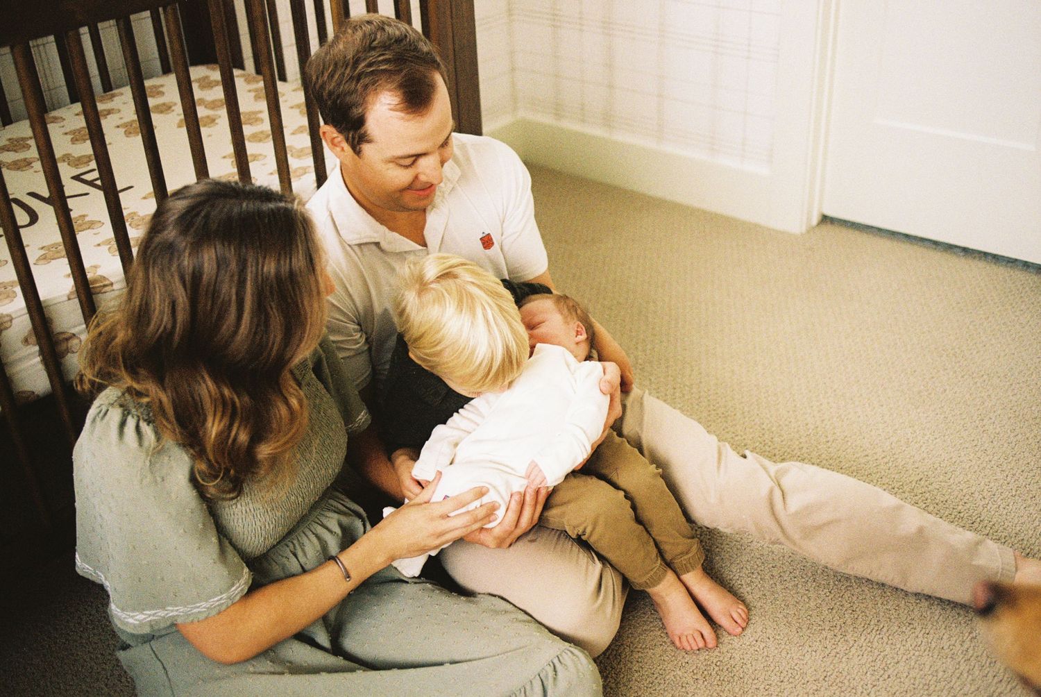 A parent holds and comforts a small infant while sitting on a carpeted floor.