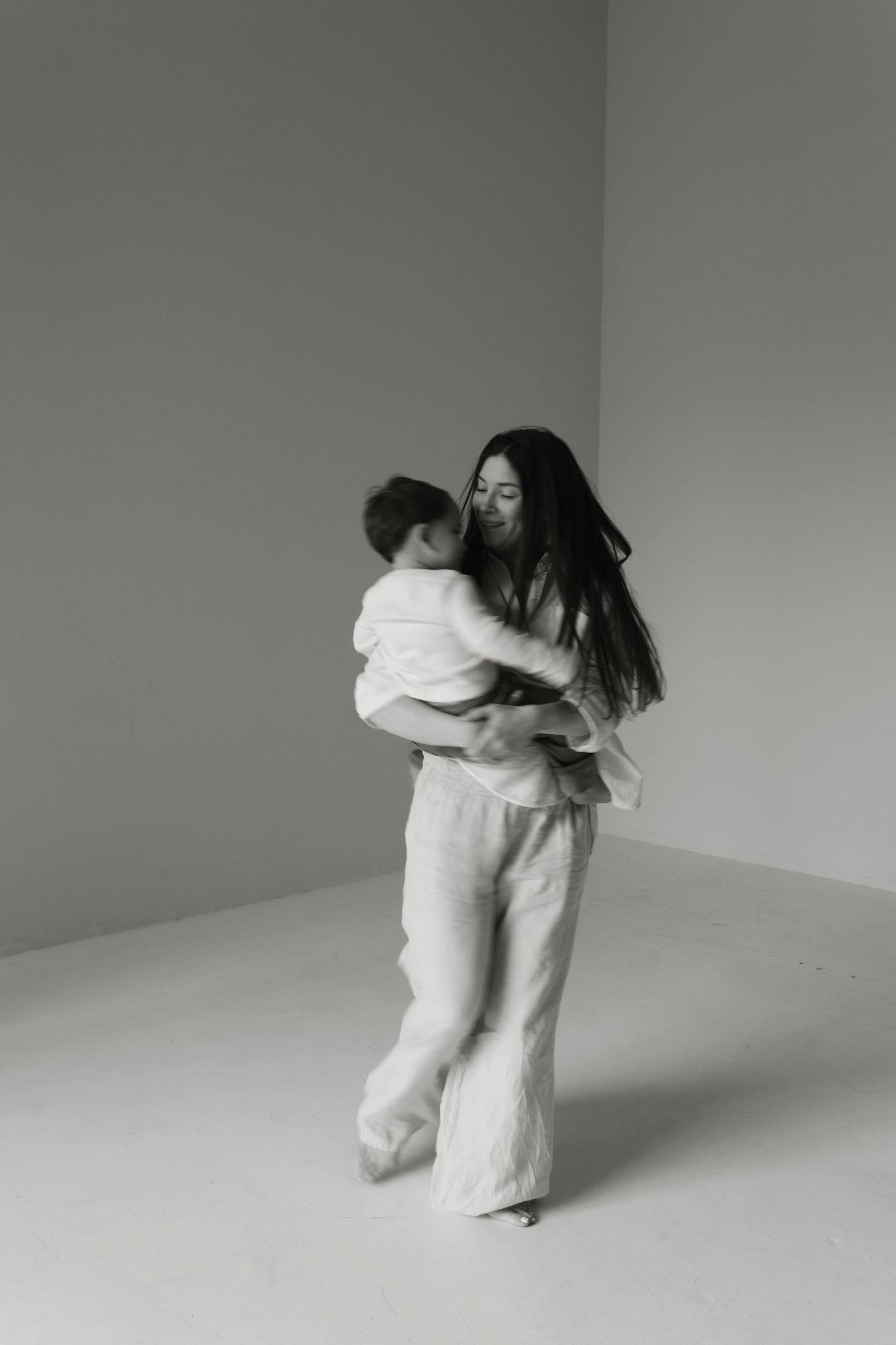Documentary motherhood photo of a mom tickling her son during a minimalist white studio session.