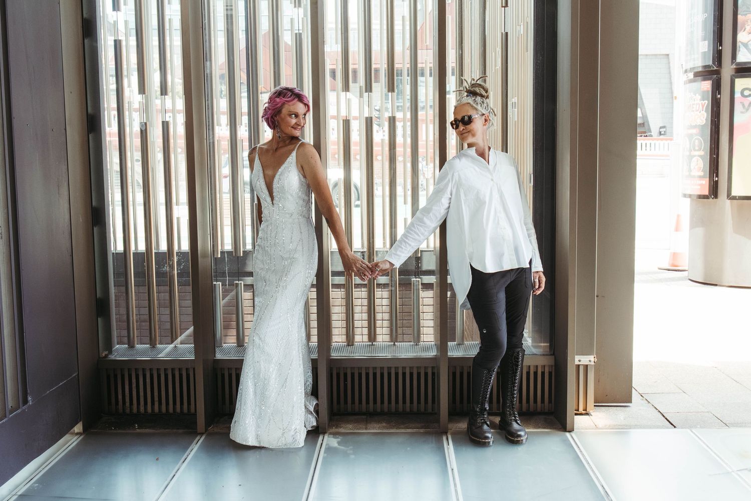 Wives hold hands across interesting backdrop.