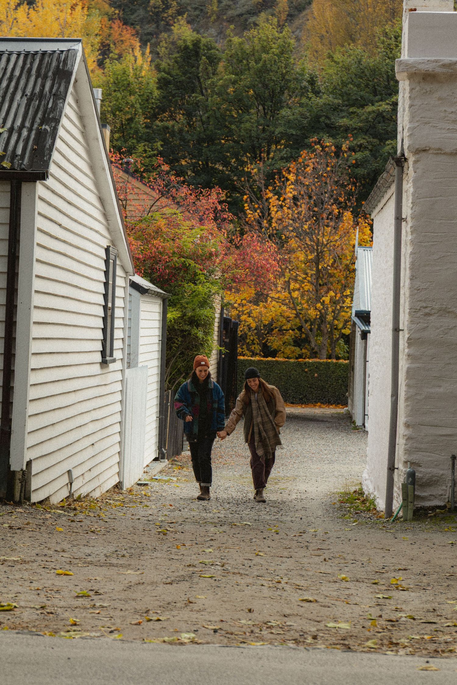 Couple walking hand in hand down a narrow cobblestone alley between white buildings with colorful autumn trees.