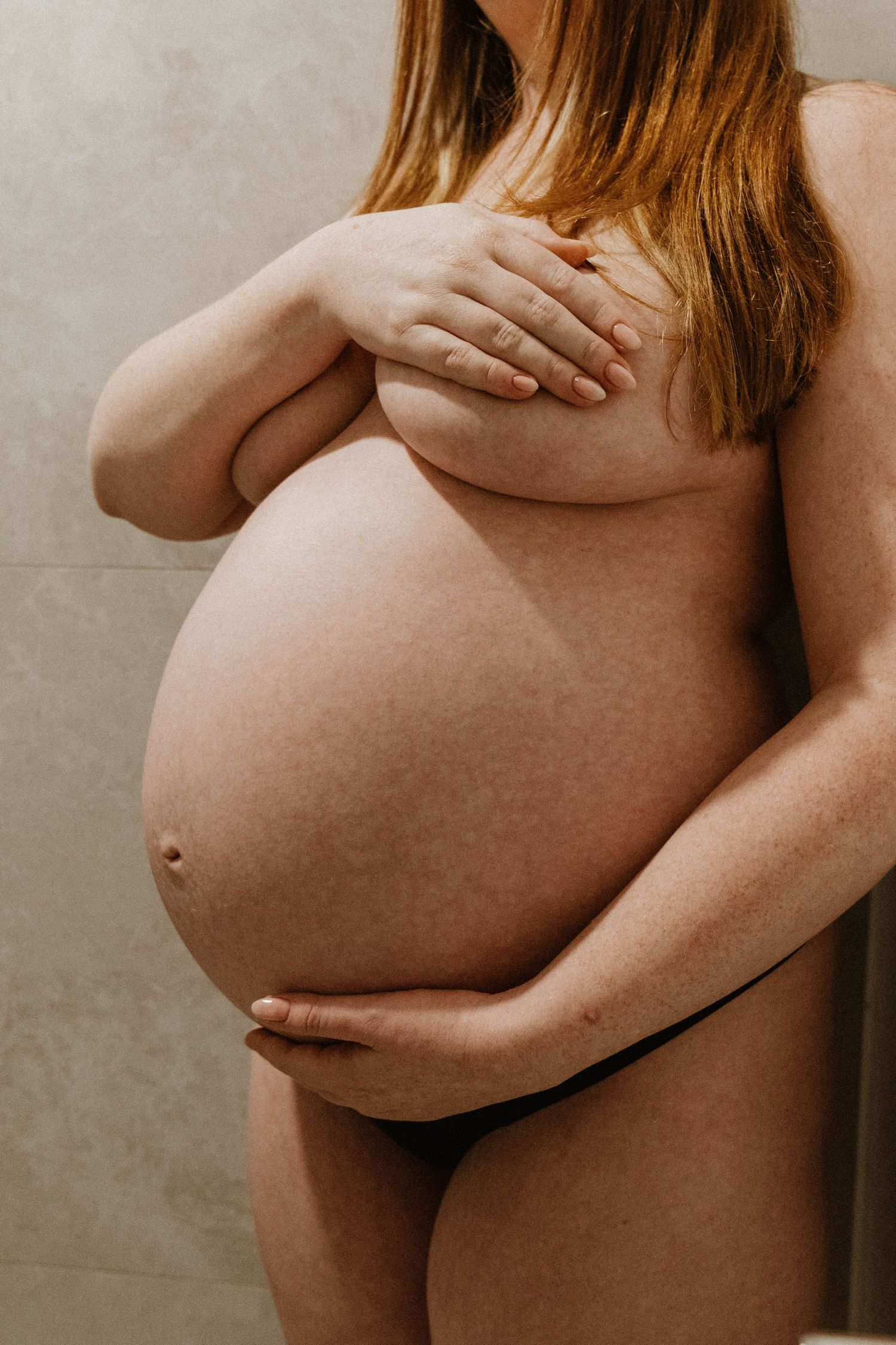 Orange haired woman caressing pregnant belly.