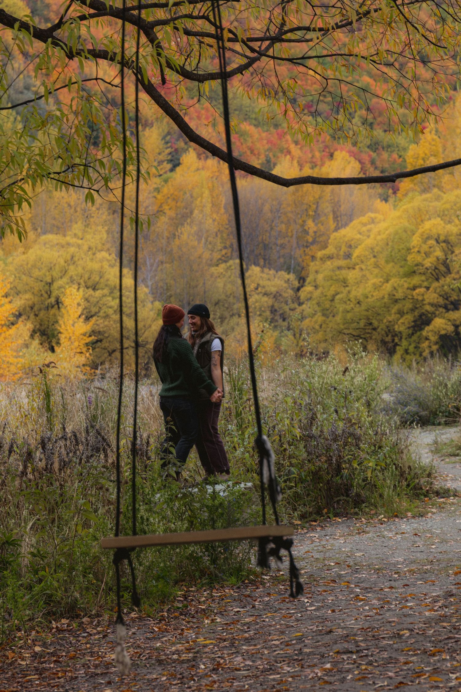 Couple embracing near a wooden swing in an autumn forest with vibrant yellow and red foliage.