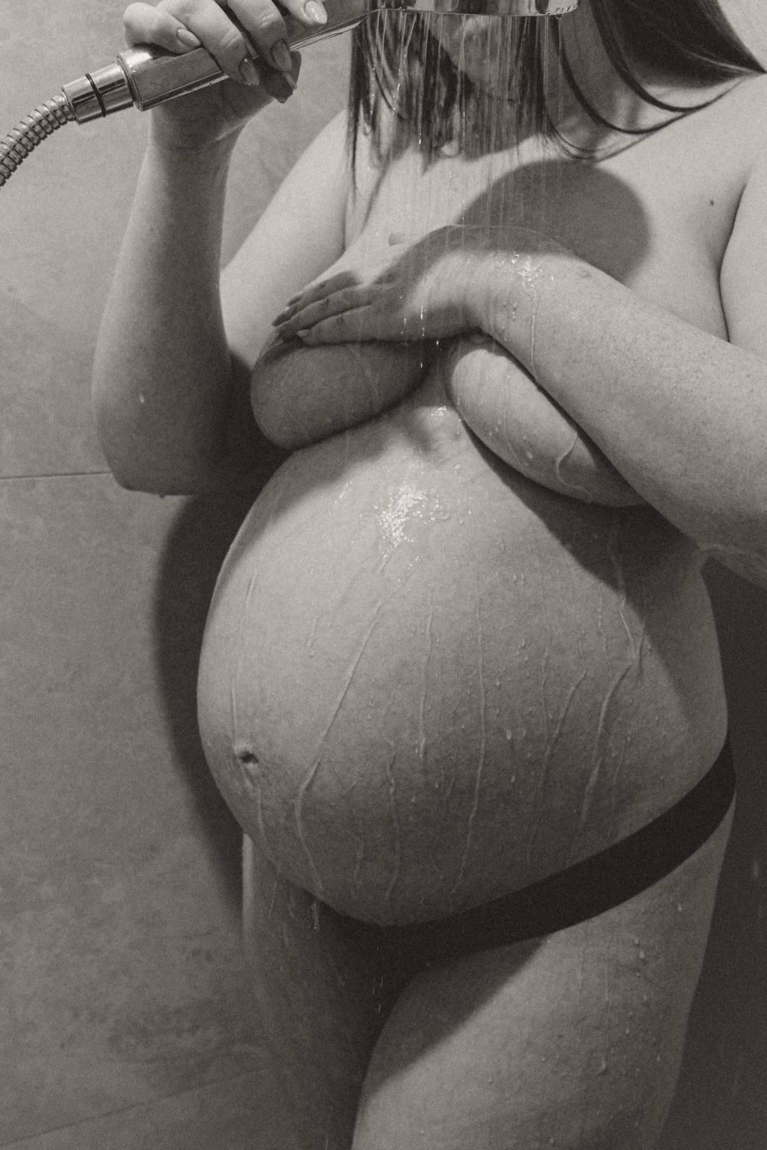 Pregnant woman uses shower head on body