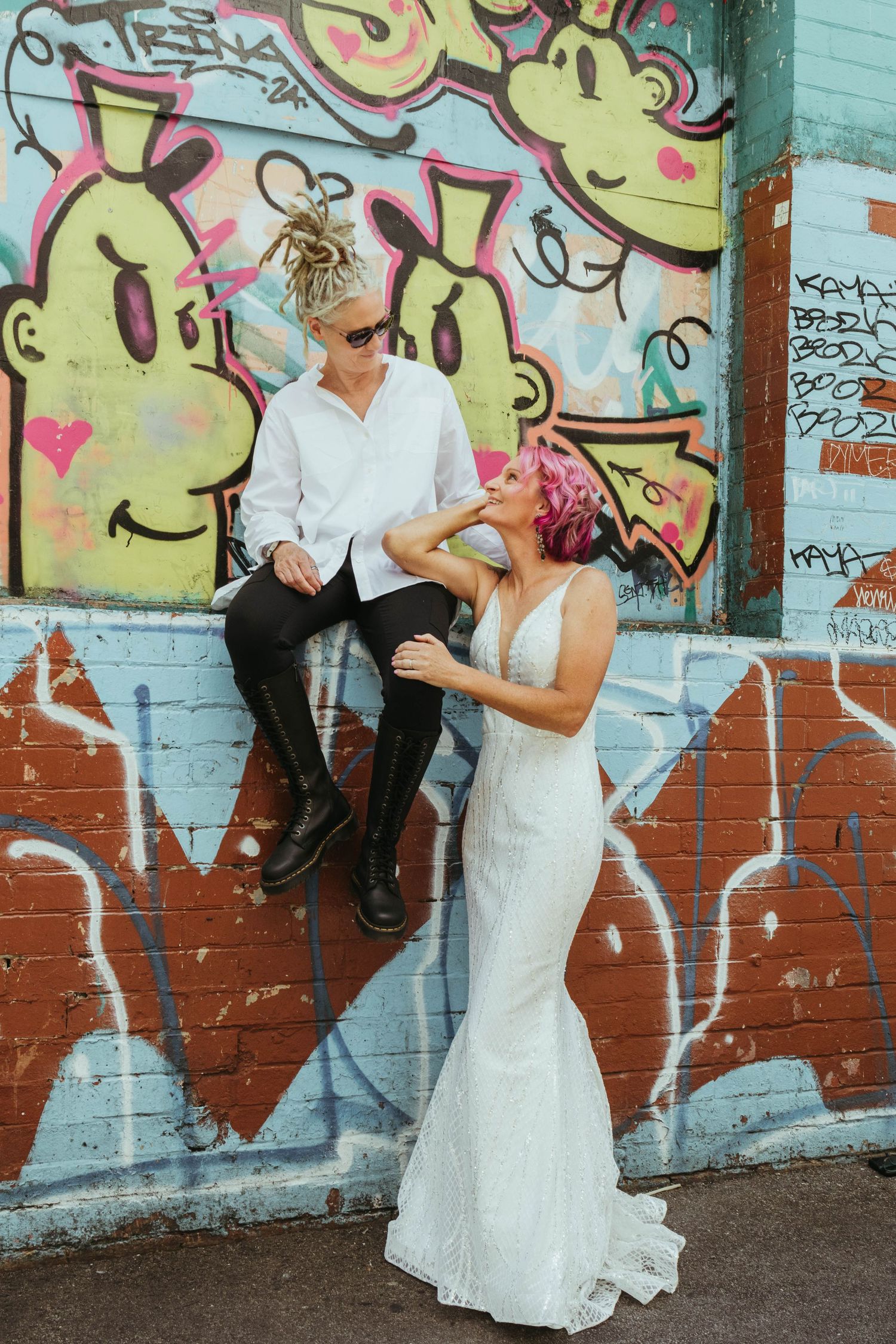 Wife seated on a wall while their wife stands below them.