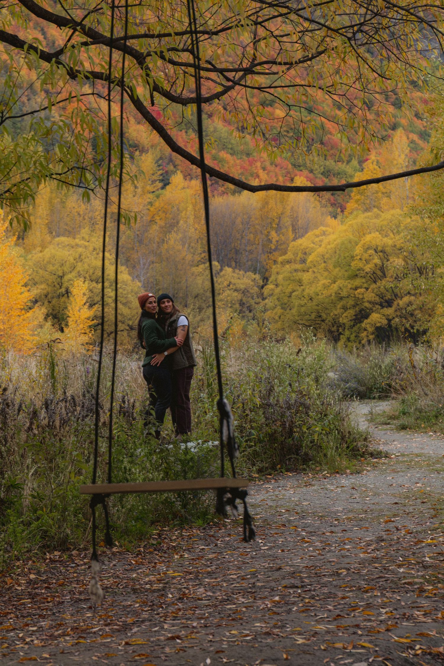 Couple embracing beside a large wooden swing surrounded by vibrant autumn foliage in a scenic park.