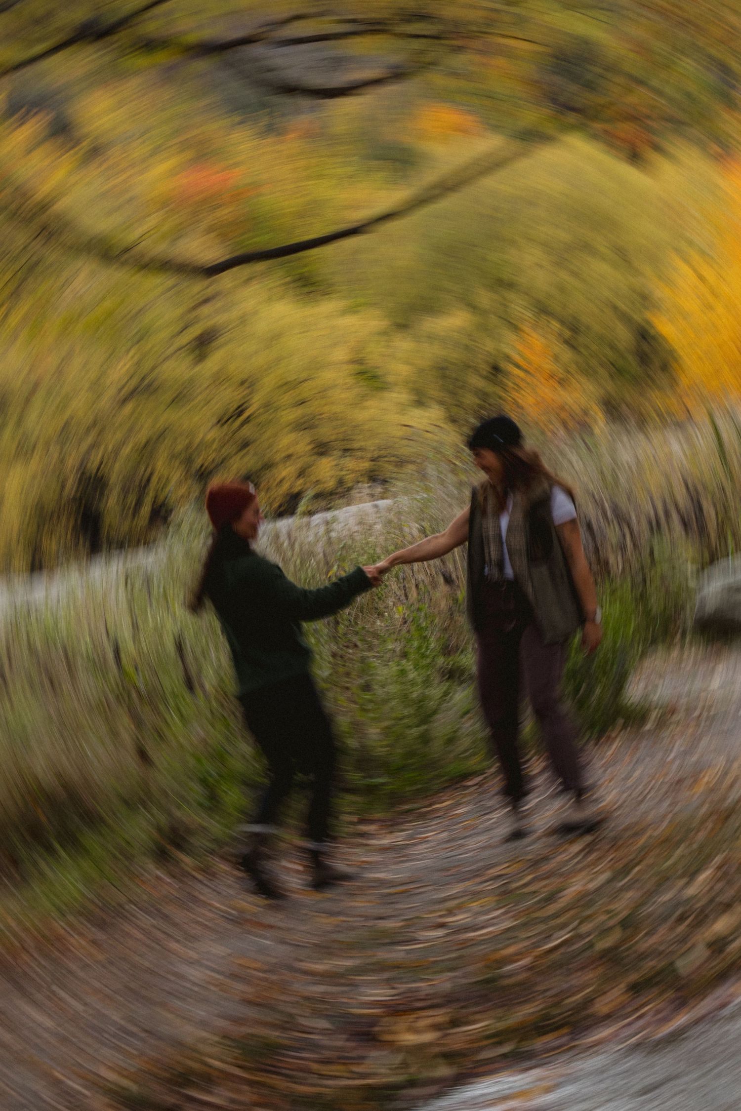 Couple holding hands on a forest path surrounded by colorful autumn foliage with a swirling spin effect.