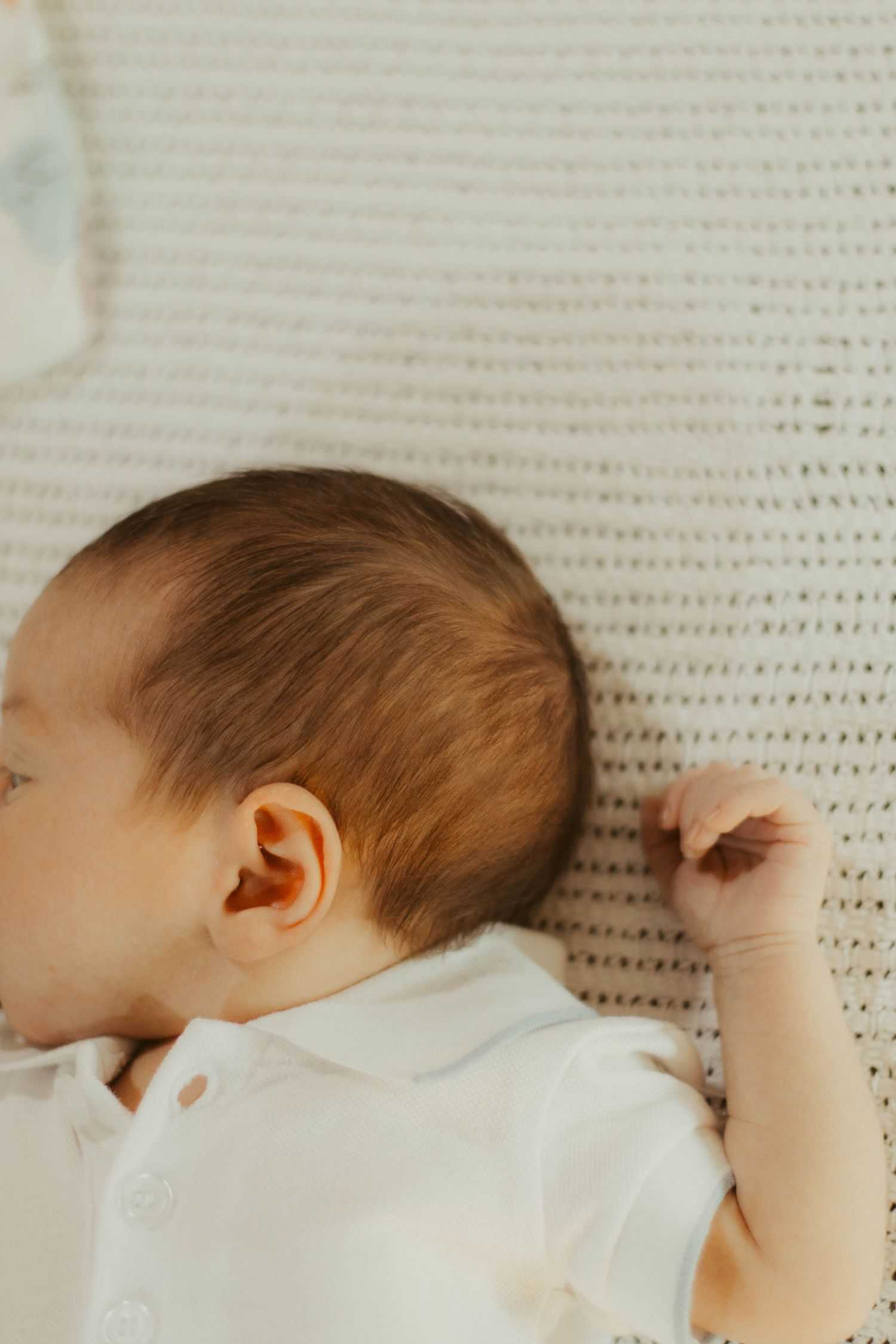 Peaceful newborn baby sleeping on a white knit blanket, wearing a white onesie, with soft brown hair.