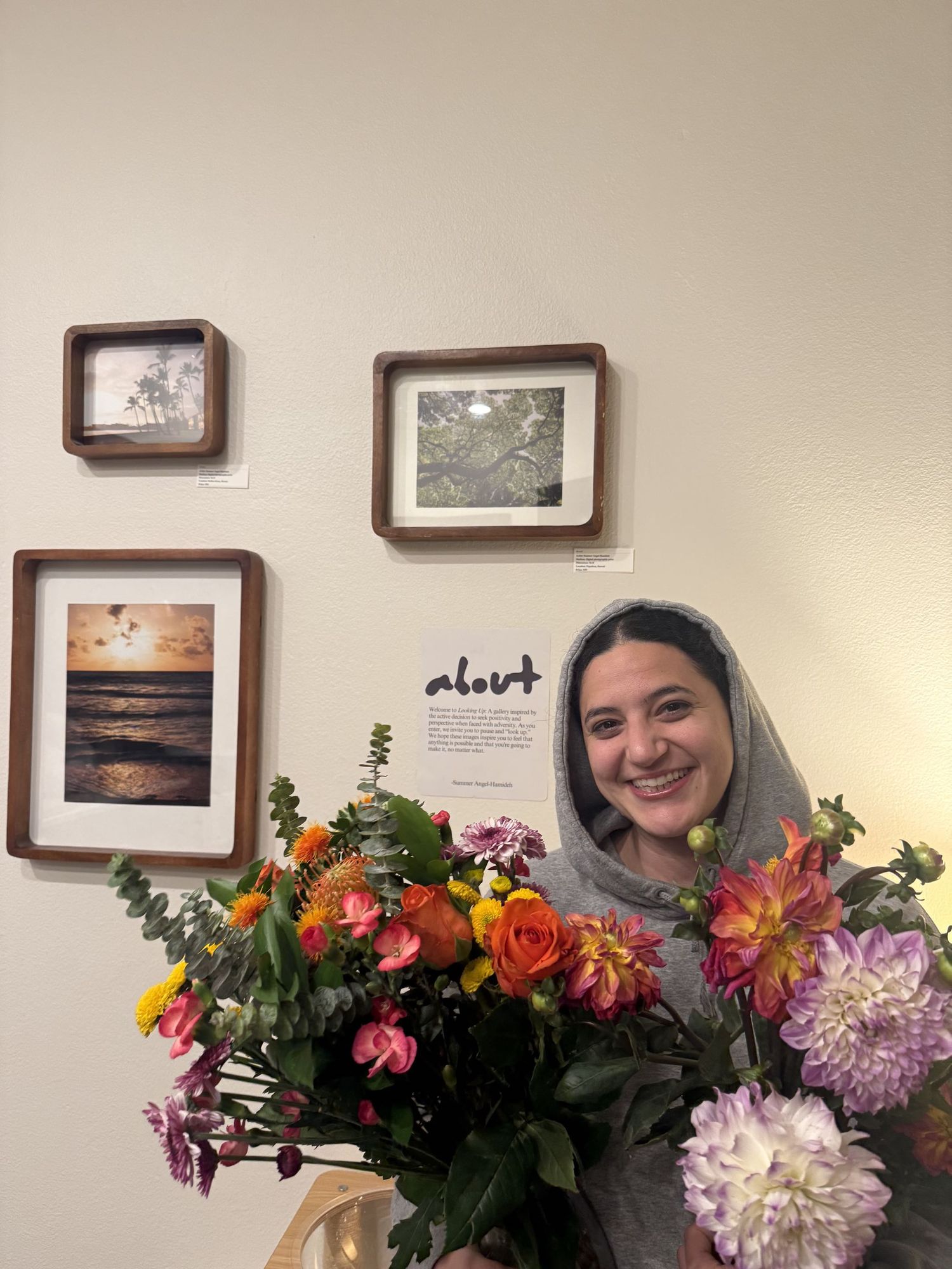 Smiling woman holding colorful bouquet of flowers standing in front of wall with framed nature photographs.