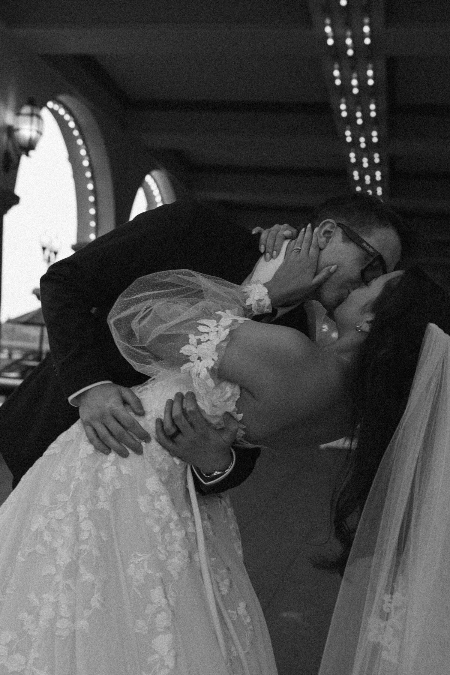 Black and white photo of a bride and groom sharing a romantic dip kiss at their wedding ceremony.