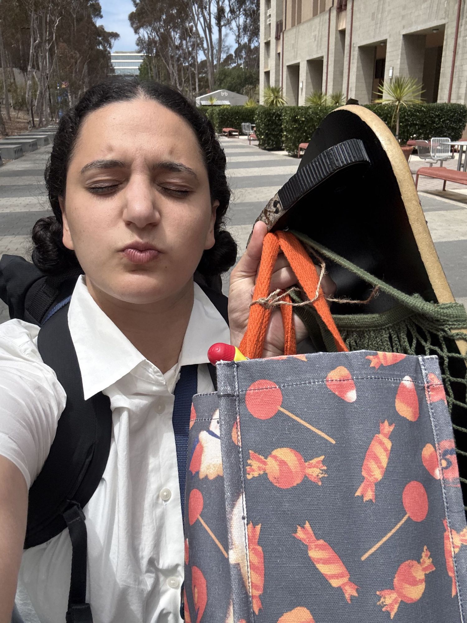 Young woman making a pouty face outdoors, holding a colorful candy-patterned bag with a Halloween Grim Reaper figure.