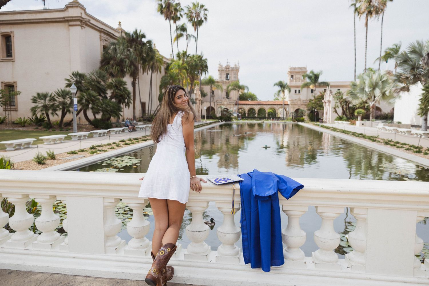 Young woman in white dress posing at Balboa Park reflecting pool in San Diego.