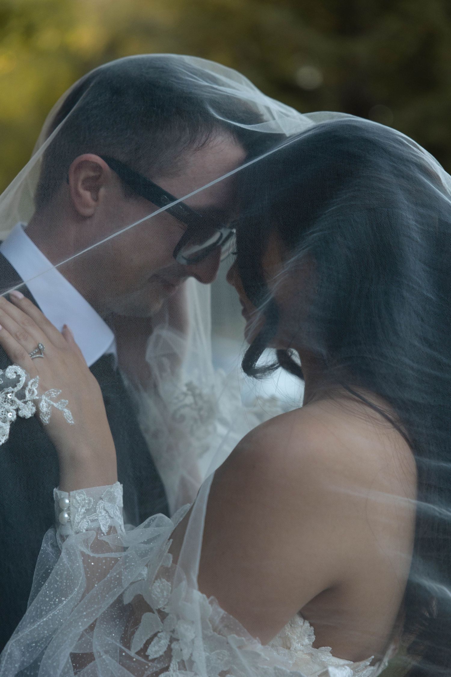Intimate close-up of bride and groom touching foreheads under a sheer veil, groom wearing glasses.
