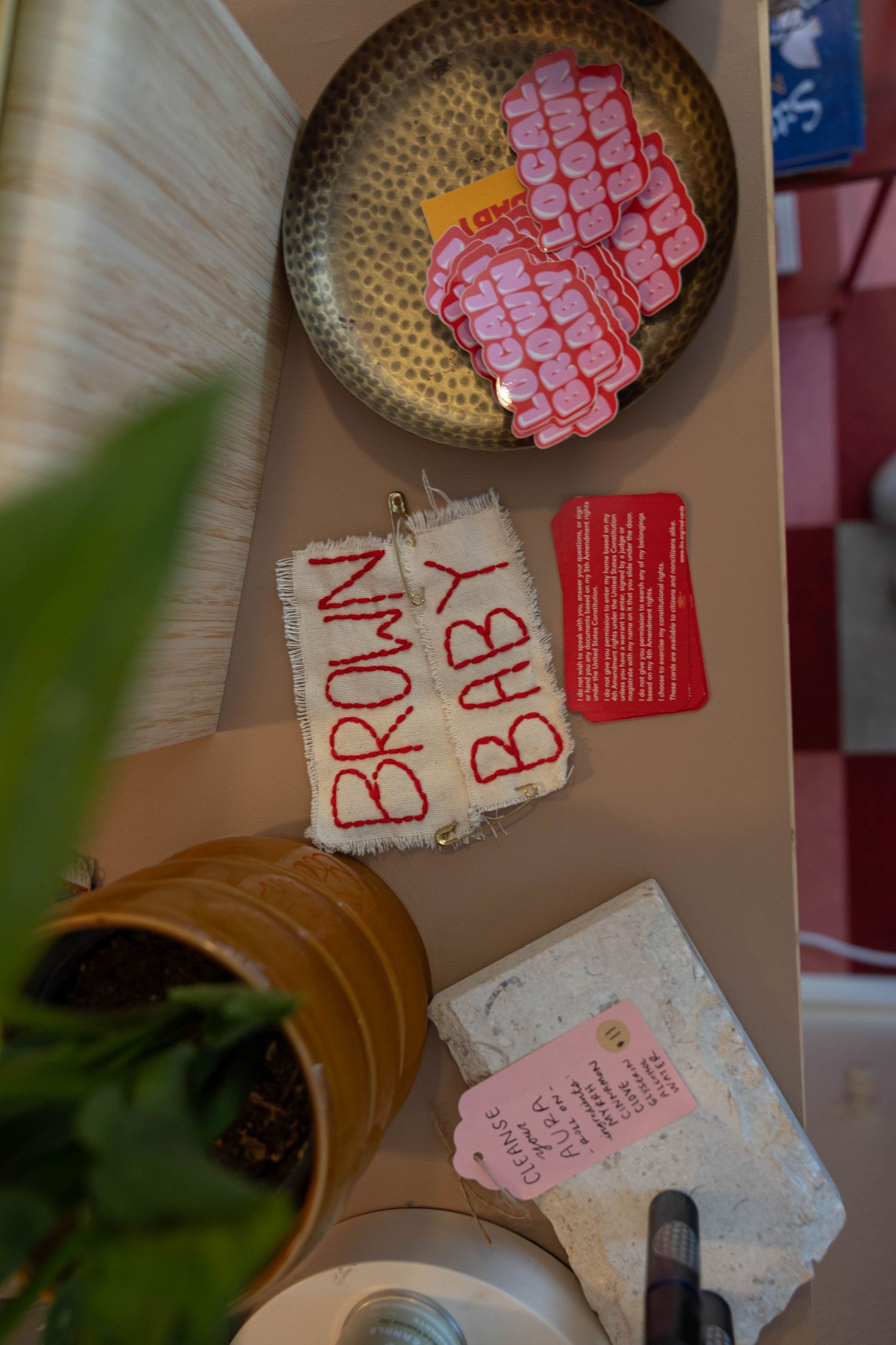 Shelf display featuring Brown Baby embroidered patch, pink button accessories in bowl, and red info cards in shop.