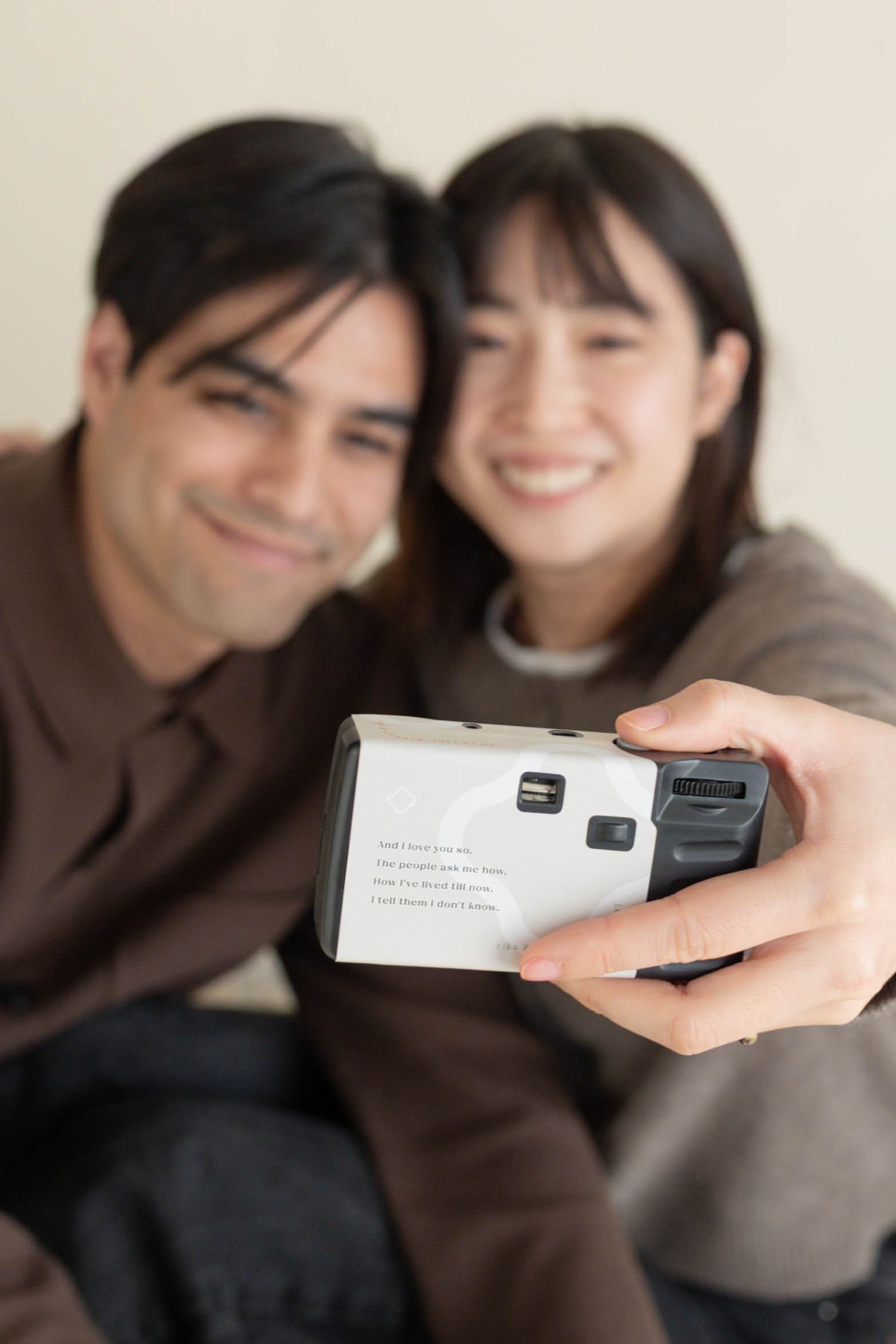 Smiling couple taking a selfie with a disposable camera, man and woman posing together in casual clothing.
