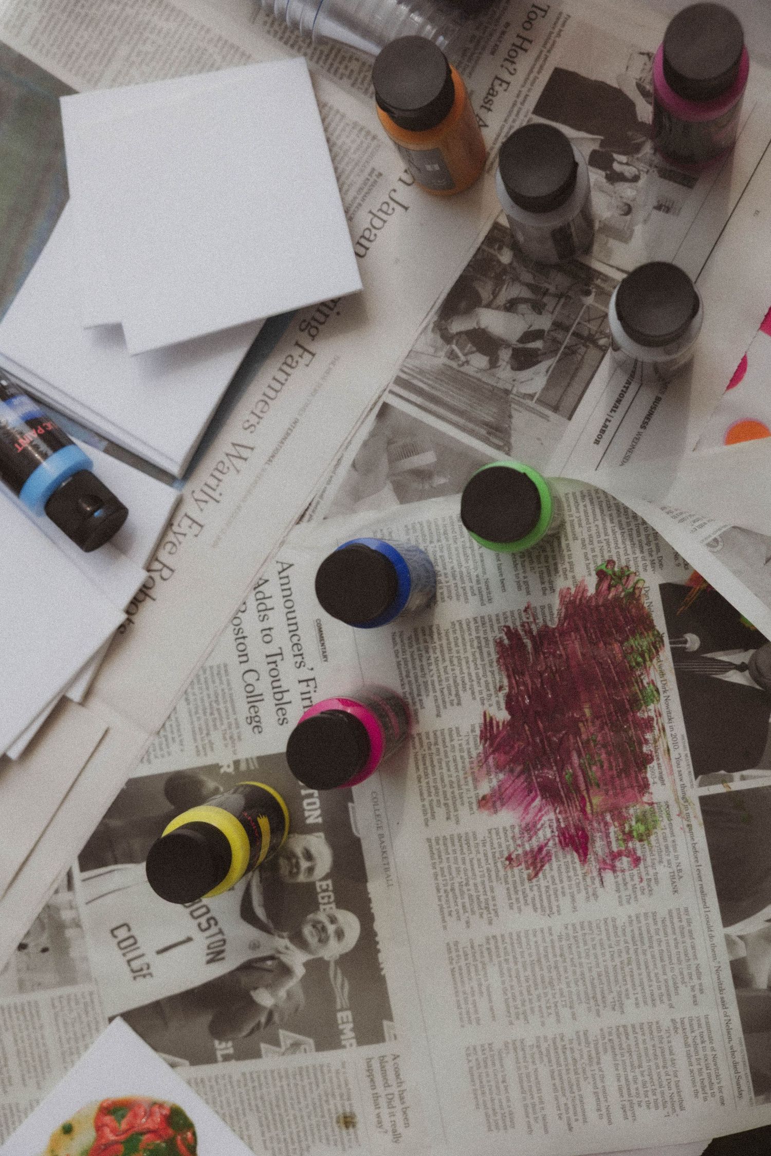 Colorful paint tubes scattered on newspaper with a paint-stained palette and blank white canvases in an artist's workspace.