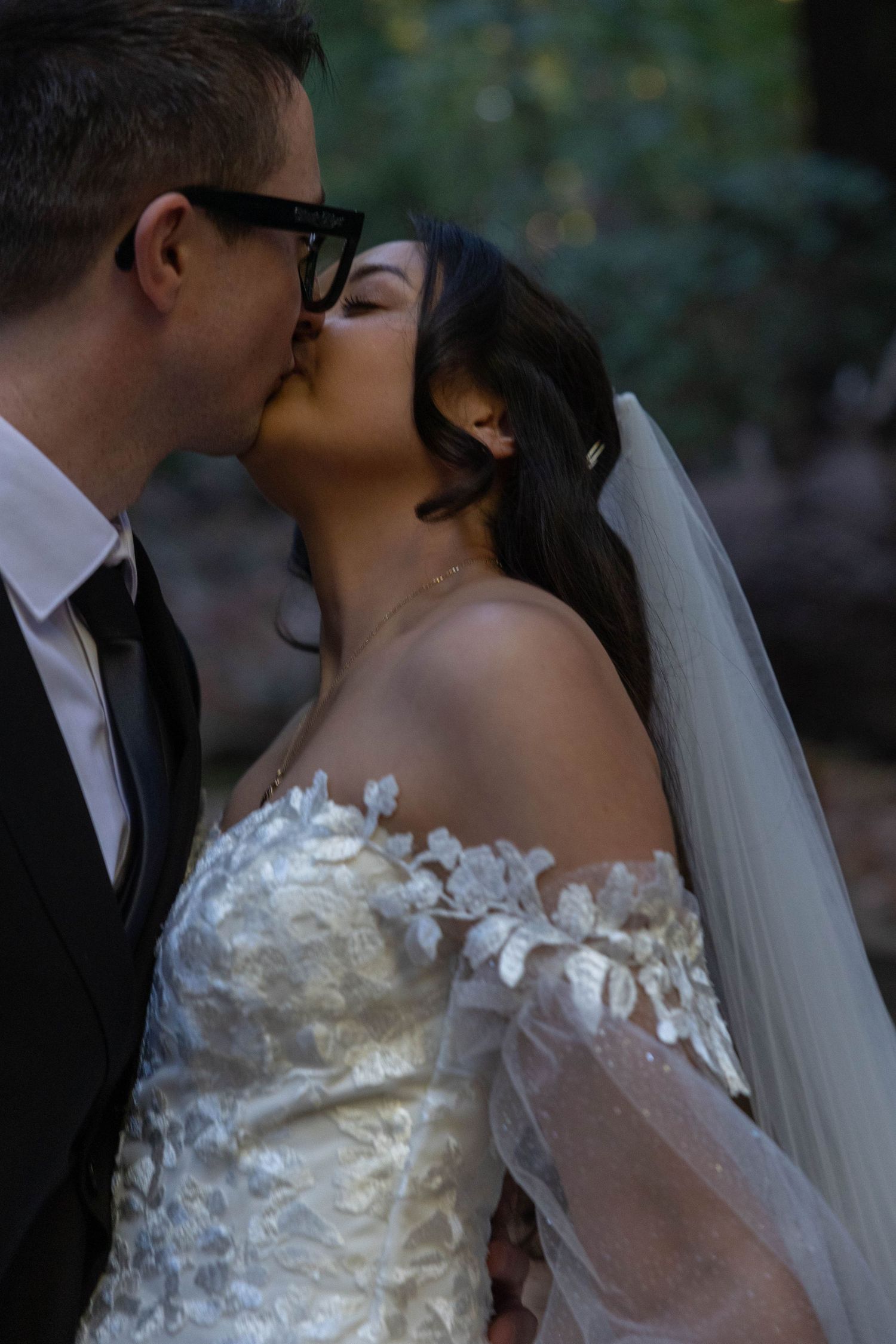 Bride and groom sharing a romantic kiss, bride wearing an off-shoulder lace wedding dress with veil. Wedding photography.