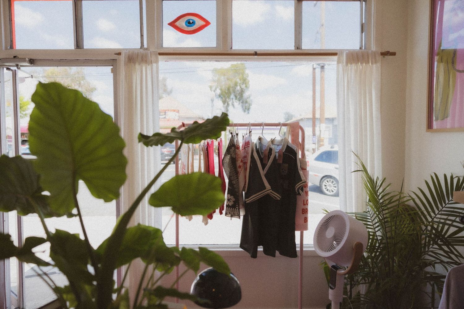Bright boutique interior with clothing rack, tropical plants, and eye window decal.