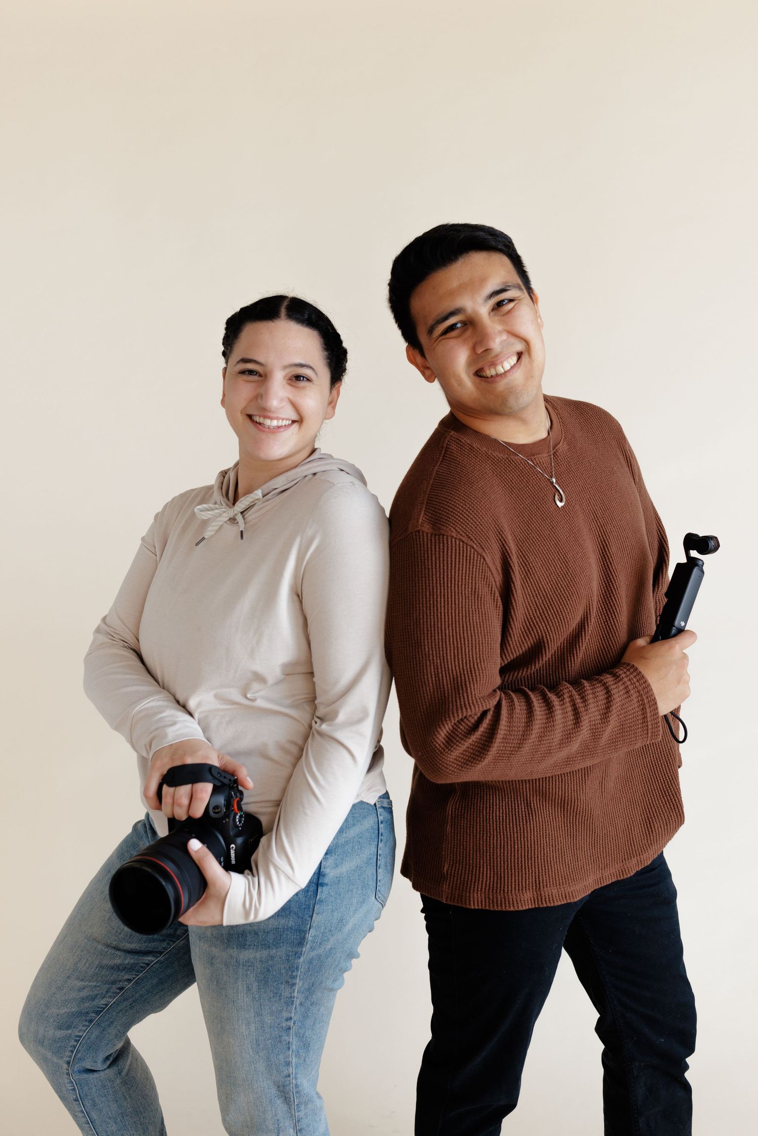 Smiling female photographer with mirrorless Canon camera and male videographer with gimbal stabilizer osmo pocket 3 camera.