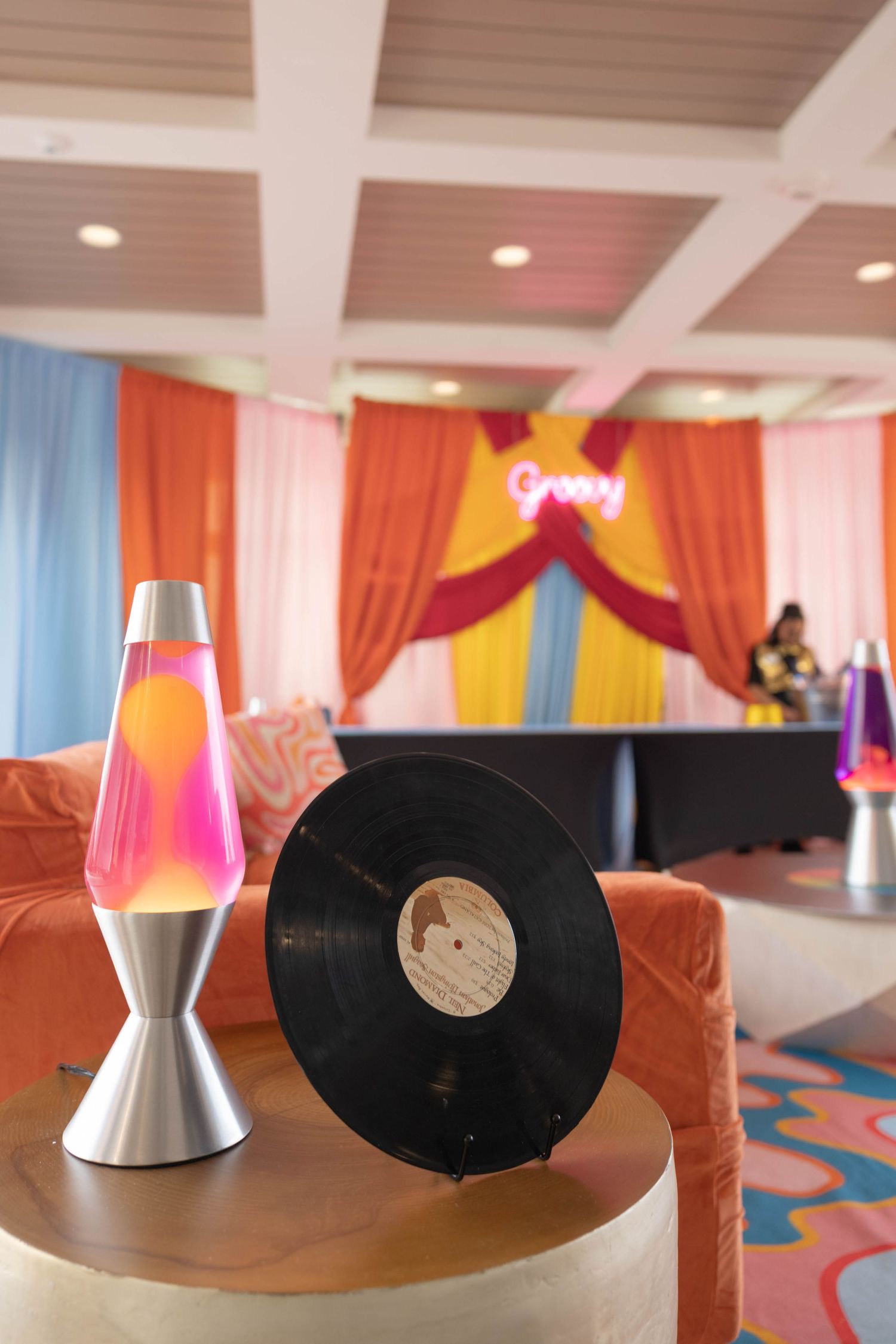 Retro groovy party venue with colorful curtain backdrop, lava lamp, vinyl record, and psychedelic wavy patterned decor.