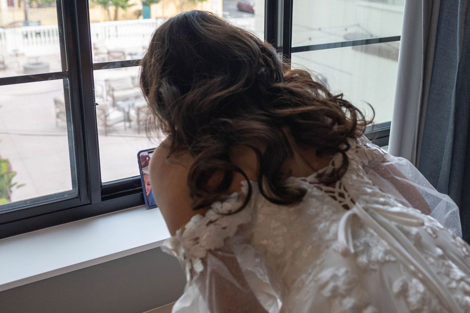 Bride in a lace wedding dress with elegant updo hairstyle gazing out a window on her wedding day. Elopement Photographer.