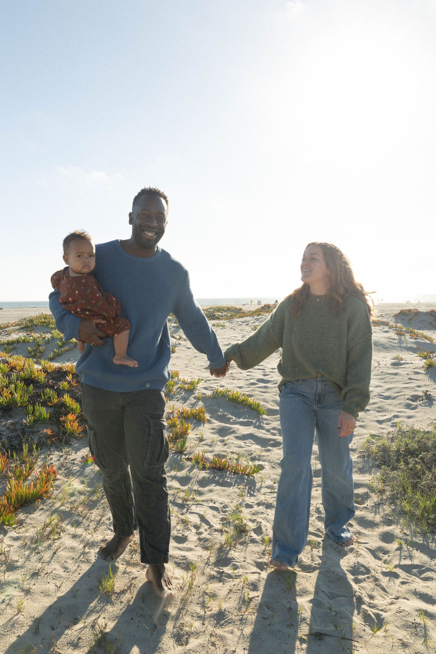 Couple and child walking on sandy beach, father holding baby while holding hands with mother on sunny day. Coronado beach family photography