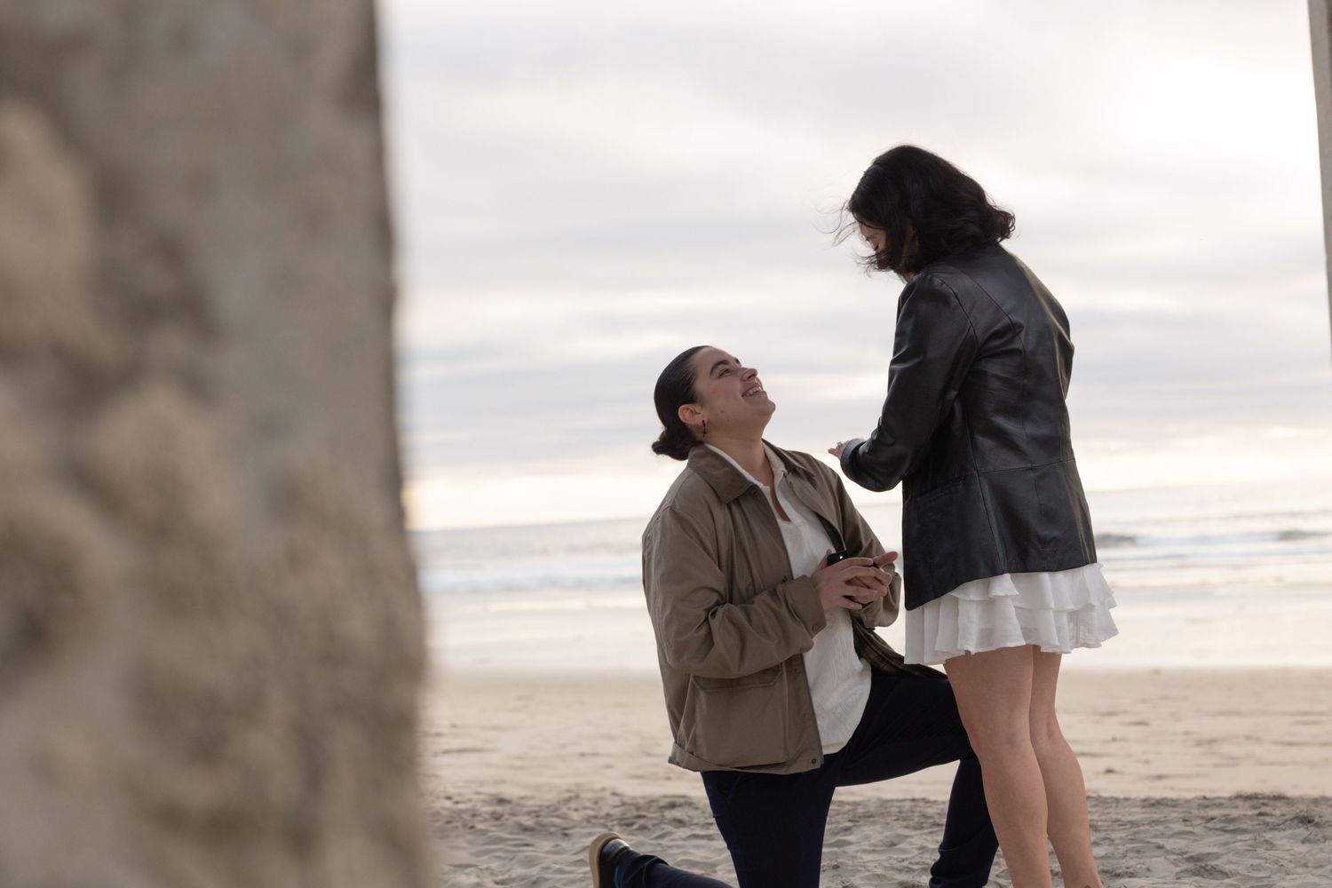 Person proposing on one knee to partner on a beach at dusk near a stone pillar. Proposal photos La Jolla Shores, San Diego, California.