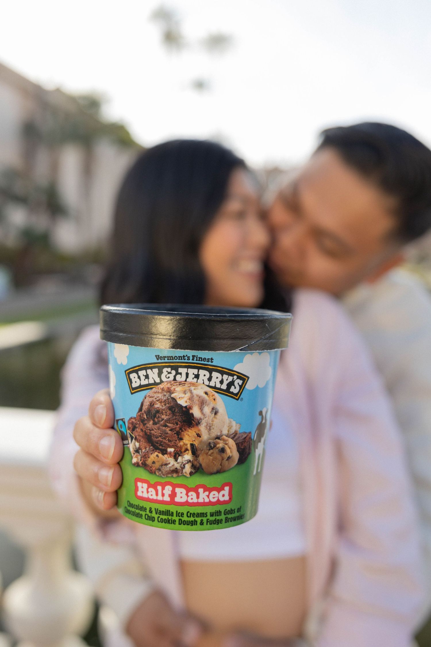 Couple sharing a romantic moment while holding a pint of Ben & Jerry's Half Baked ice cream outdoors. Maternity announcement.