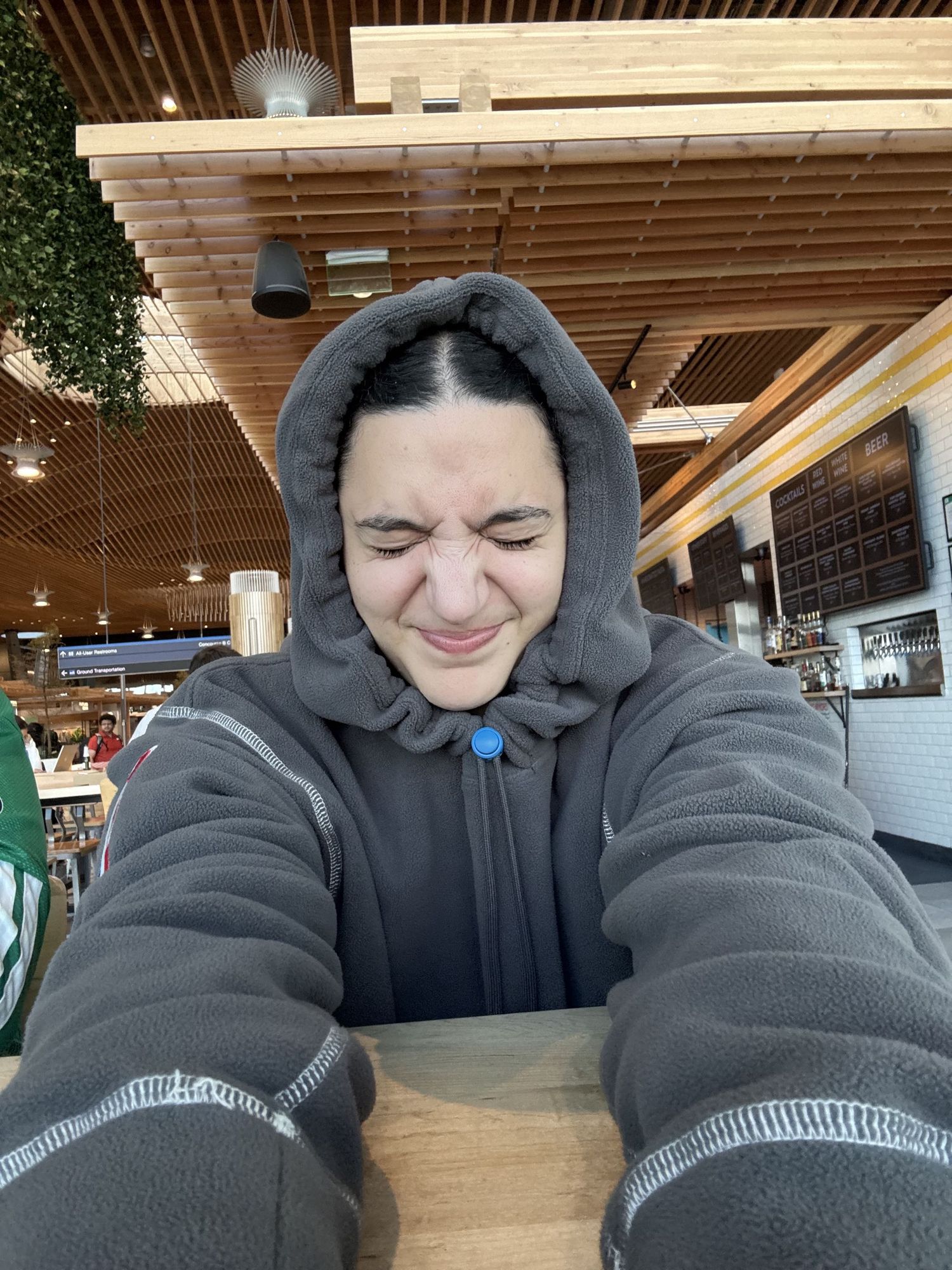 Person in gray hoodie sitting at wooden table in modern restaurant with wood ceiling.