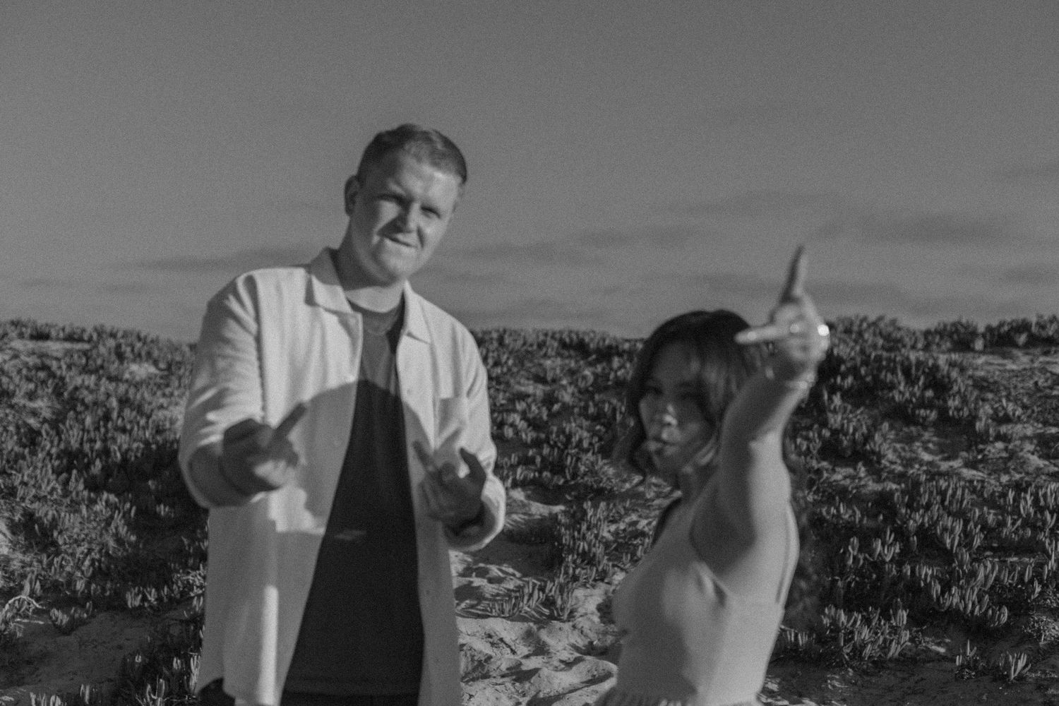 Two people posing outdoors in a field, captured in black and white photography.