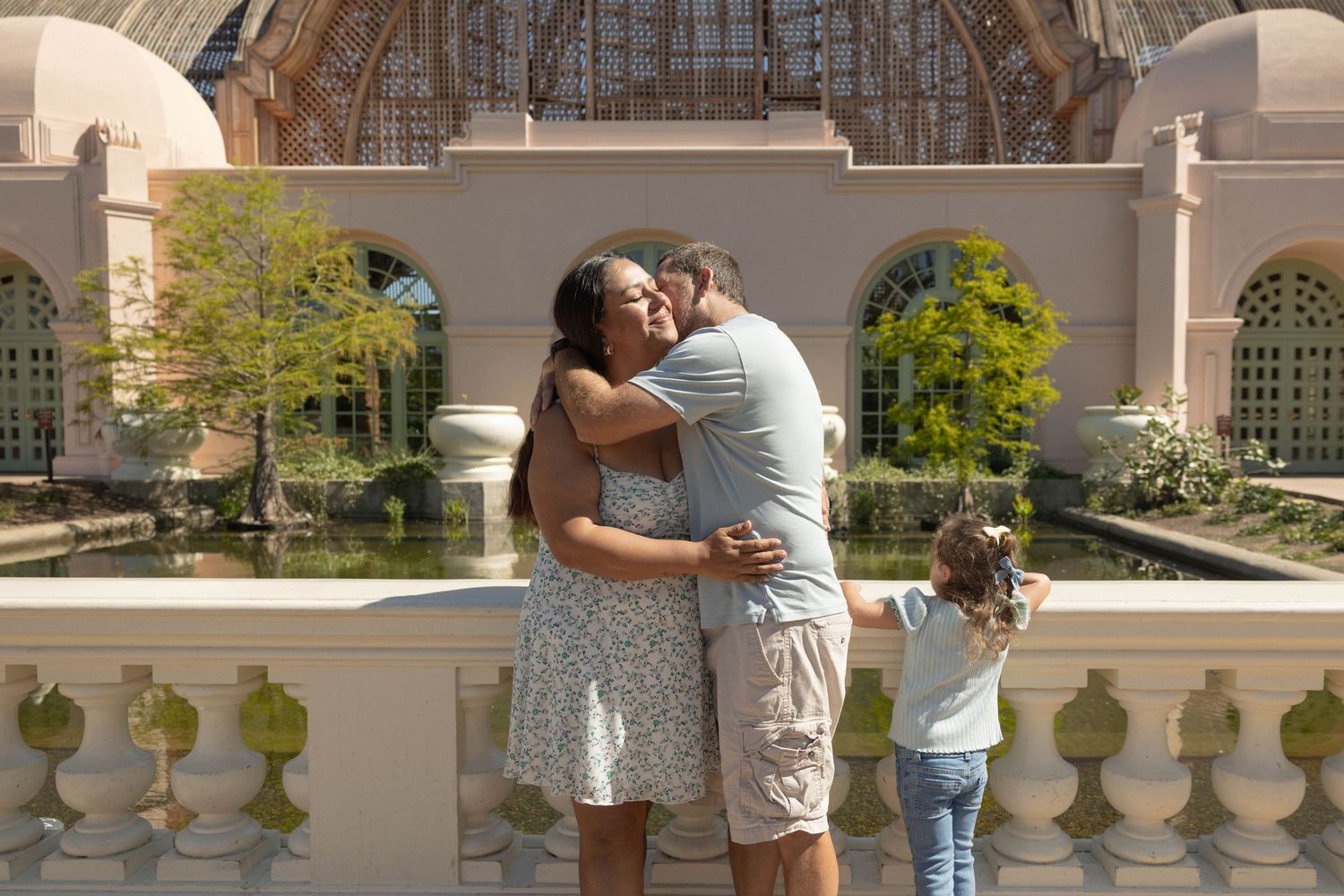 Couple embracing and kissing in front of an ornate garden building while a young child stands nearby.