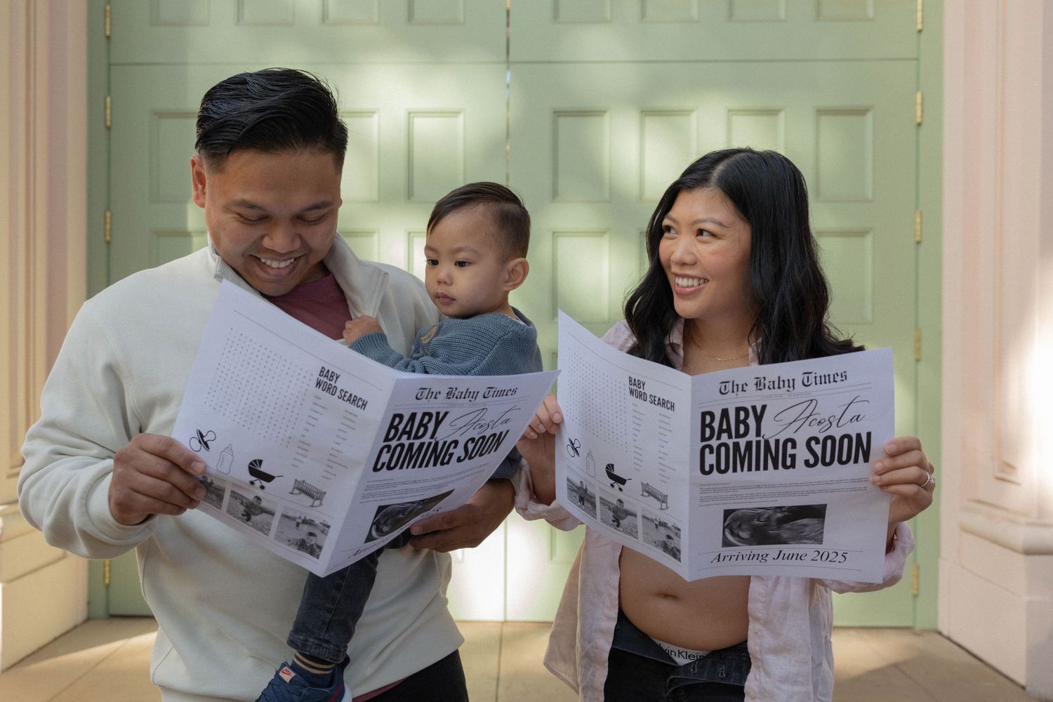 Family holding baby announcement newspapers reading Baby Coming Soon, with parents smiling and holding their infant child. maternity photos.