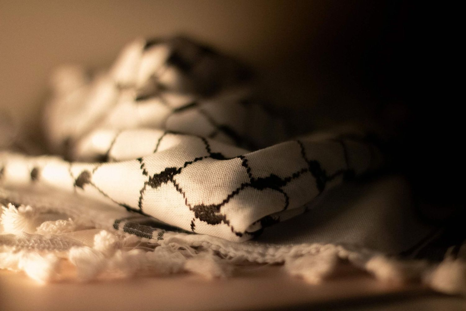 Warm-toned close-up of a folded black and white checkered keffiyeh scarf on a lace surface.