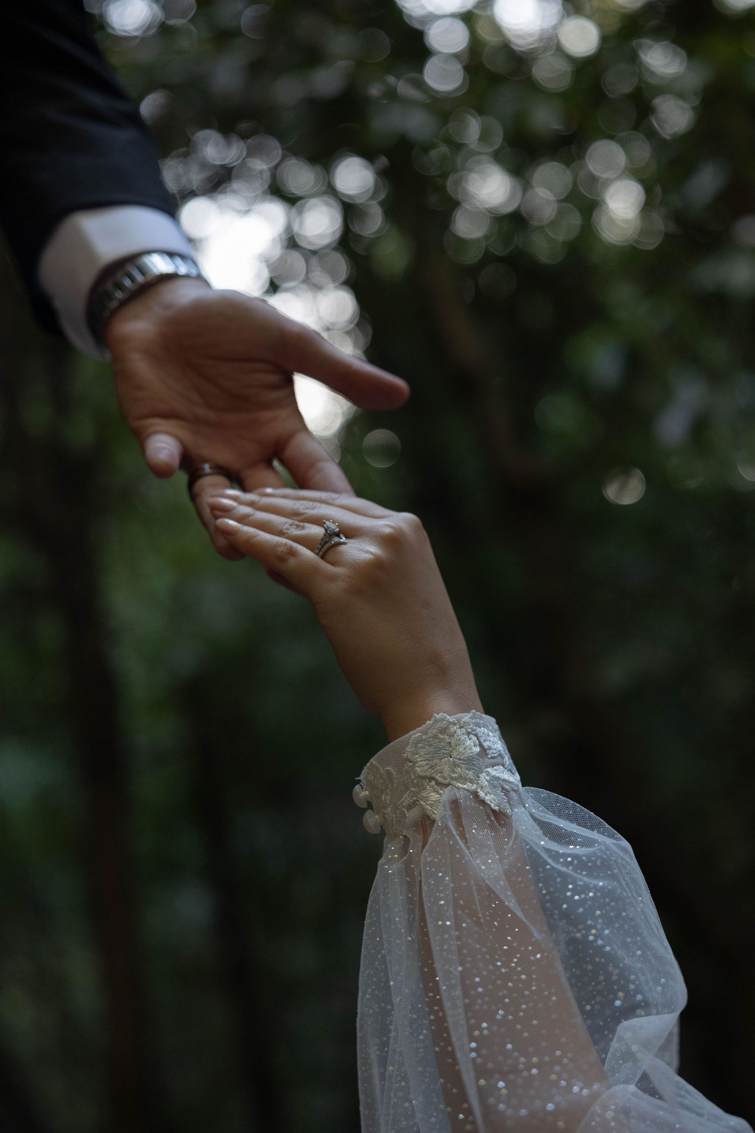 Close-up of bride and groom touching fingertips, bride wearing a diamond ring and lace wedding dress sleeve. Wedding photography.