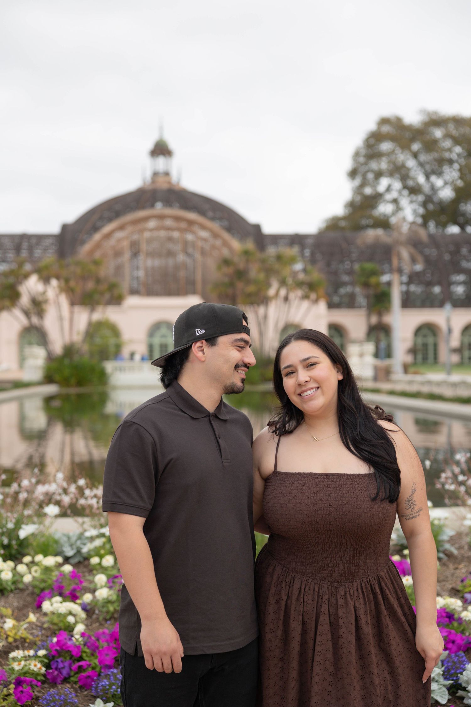 Couple smiling together in front of Balboa Park botanical building with colorful flowers in San Diego, CA. Couples Portraits.