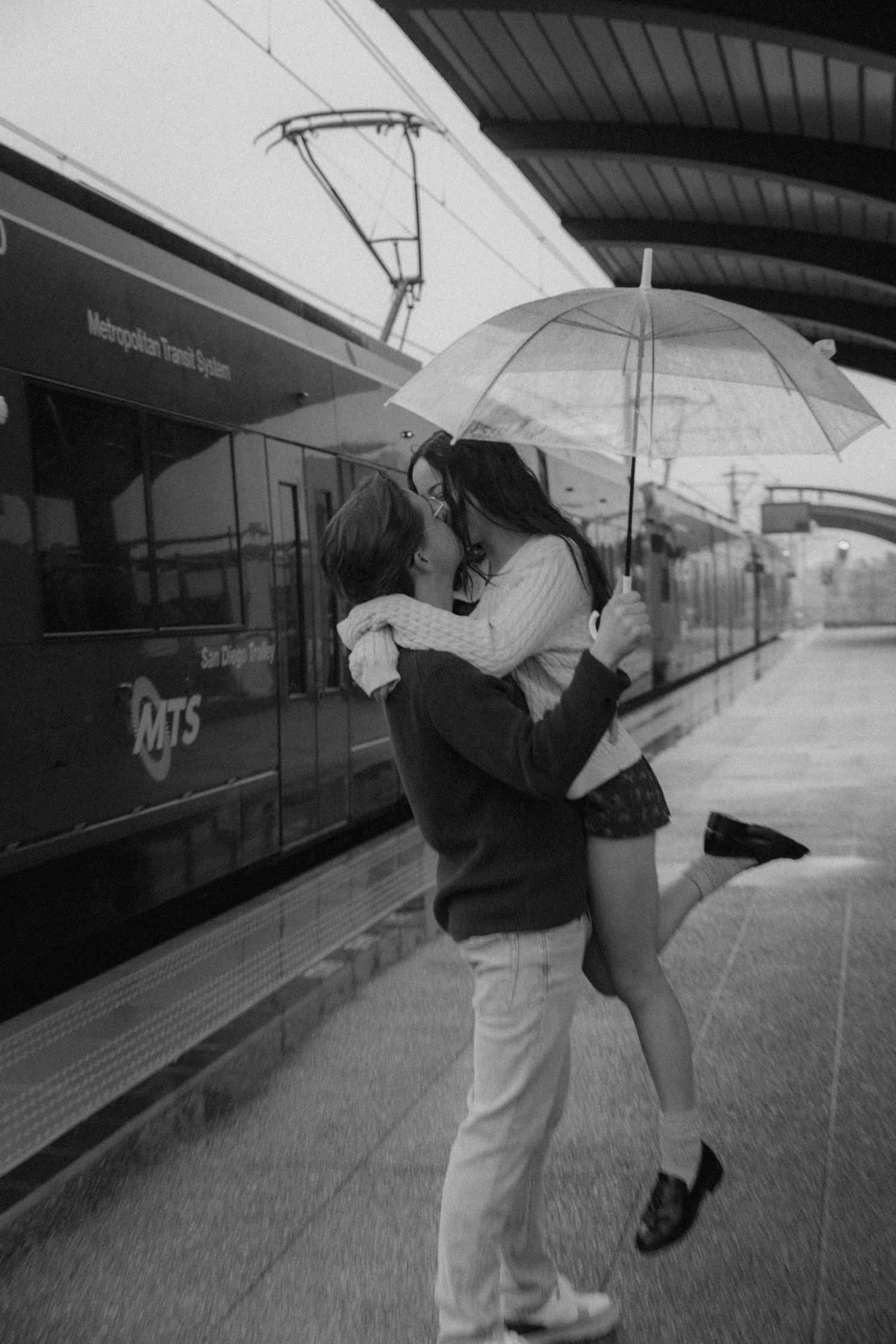 couple with umbrellas in the rain at train stop