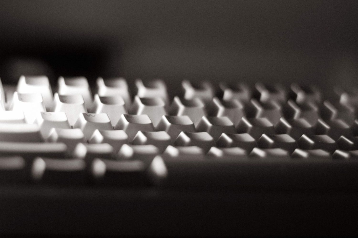 Close-up of a backlit white computer keyboard with shallow depth of field on a dark background.