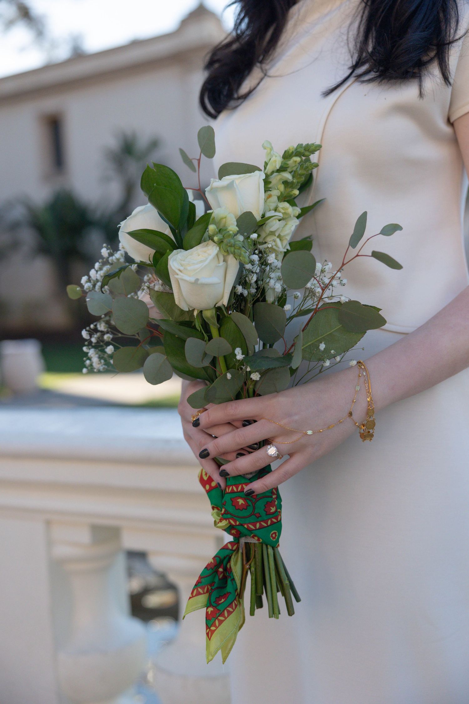 Bride in white dress holding elegant bouquet of white roses, eucalyptus, and baby's breath tied with colorful green scarf. Wedding Photos.