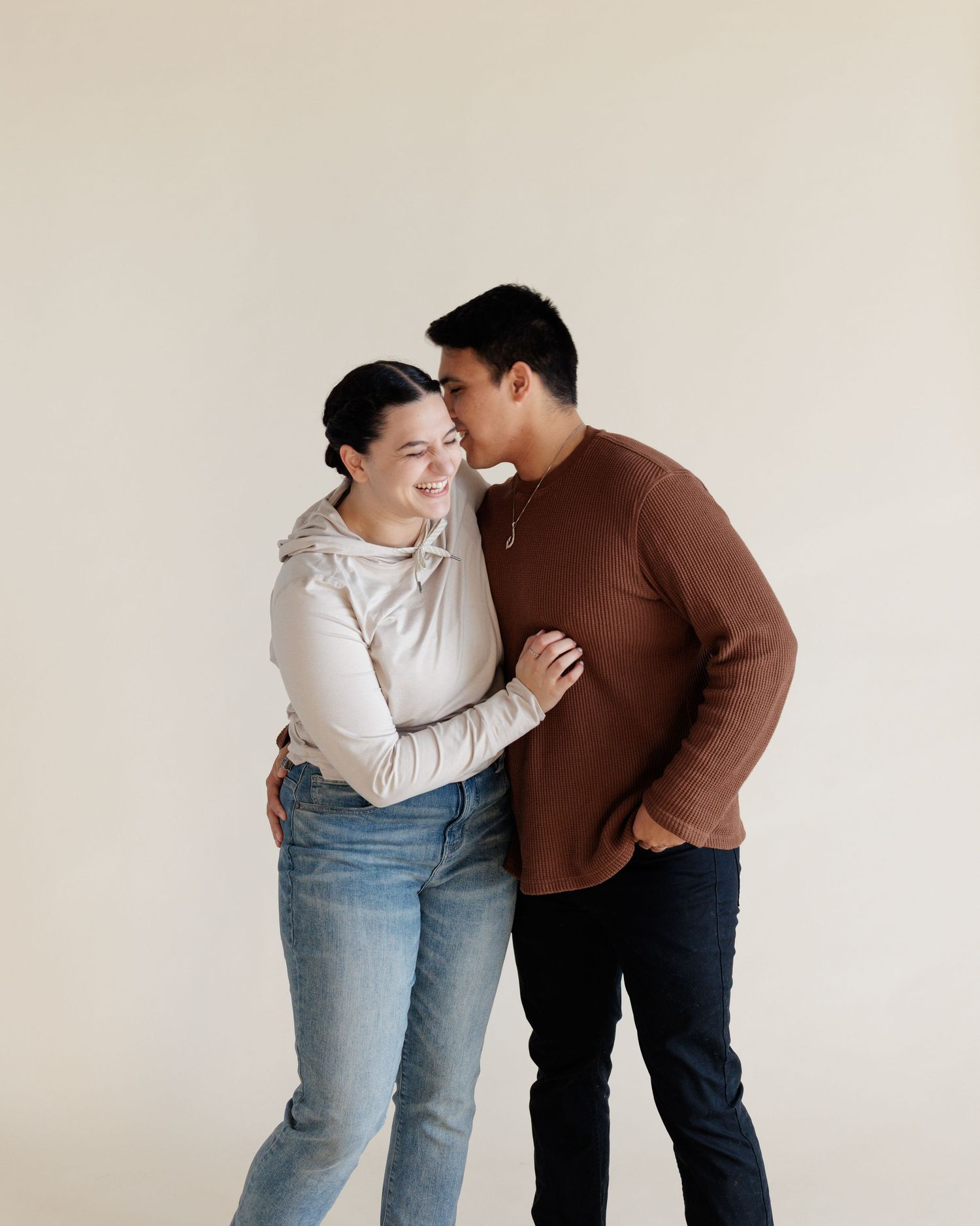 couple laughing and hugging wearing casual clothes infront of photography backdrop.