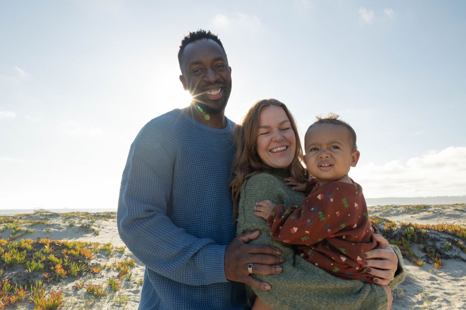 Happy family with baby smiling together on a sunny beach, enjoying a warm outdoor day by the ocean. Family Photographer.