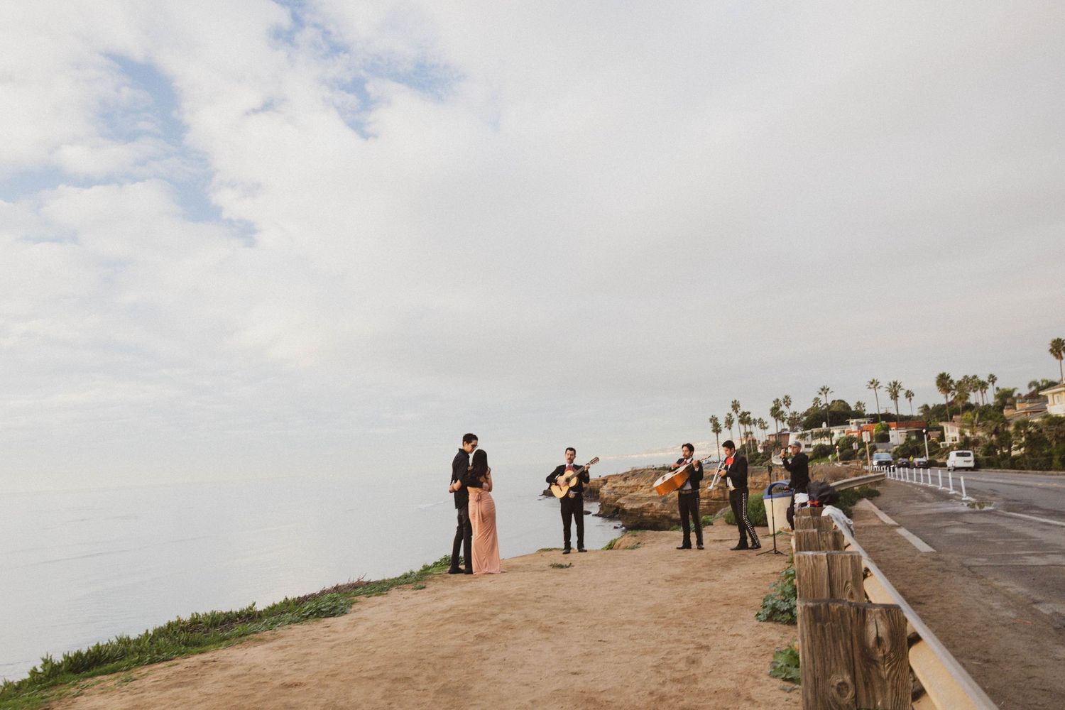 Wedding band performing on a coastal cliff overlooking the ocean under cloudy skies.