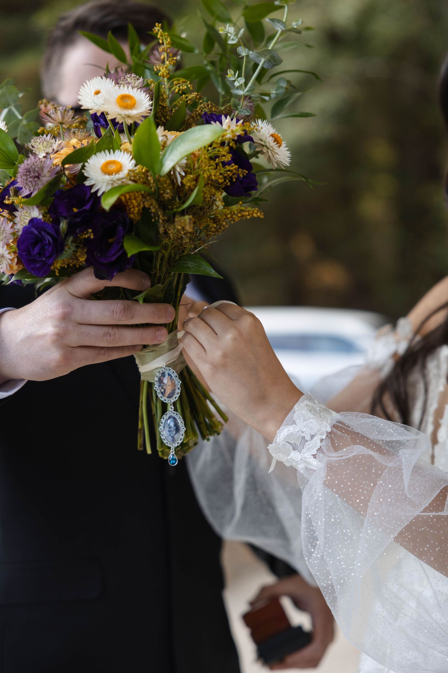 Bride and groom holding a rustic wedding bouquet with daisies, purple flowers, and greenery, bride wearing lace sleeve. Elopement Photos