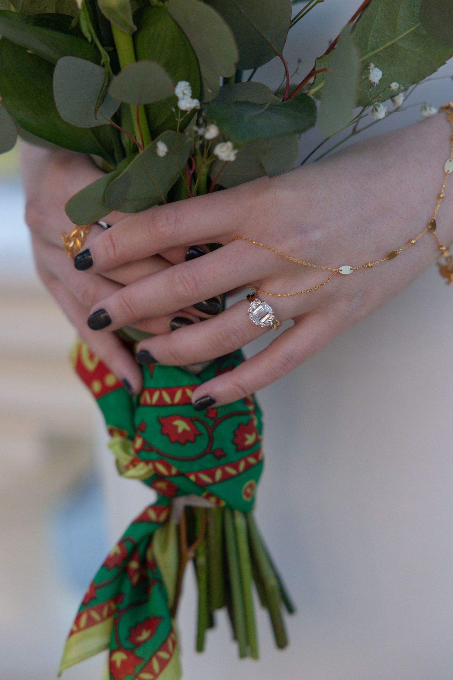 Bride holding a white rose bouquet wrapped in colorful Palestinian print fabric, wearing a diamond ring and gold bracelet.