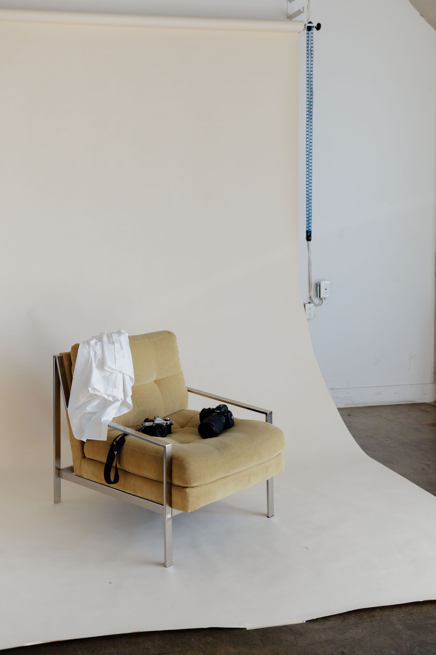 yellow velvet chair showcase draped white button up t-shirt and with camera in the studio with paper backdrop in the background.