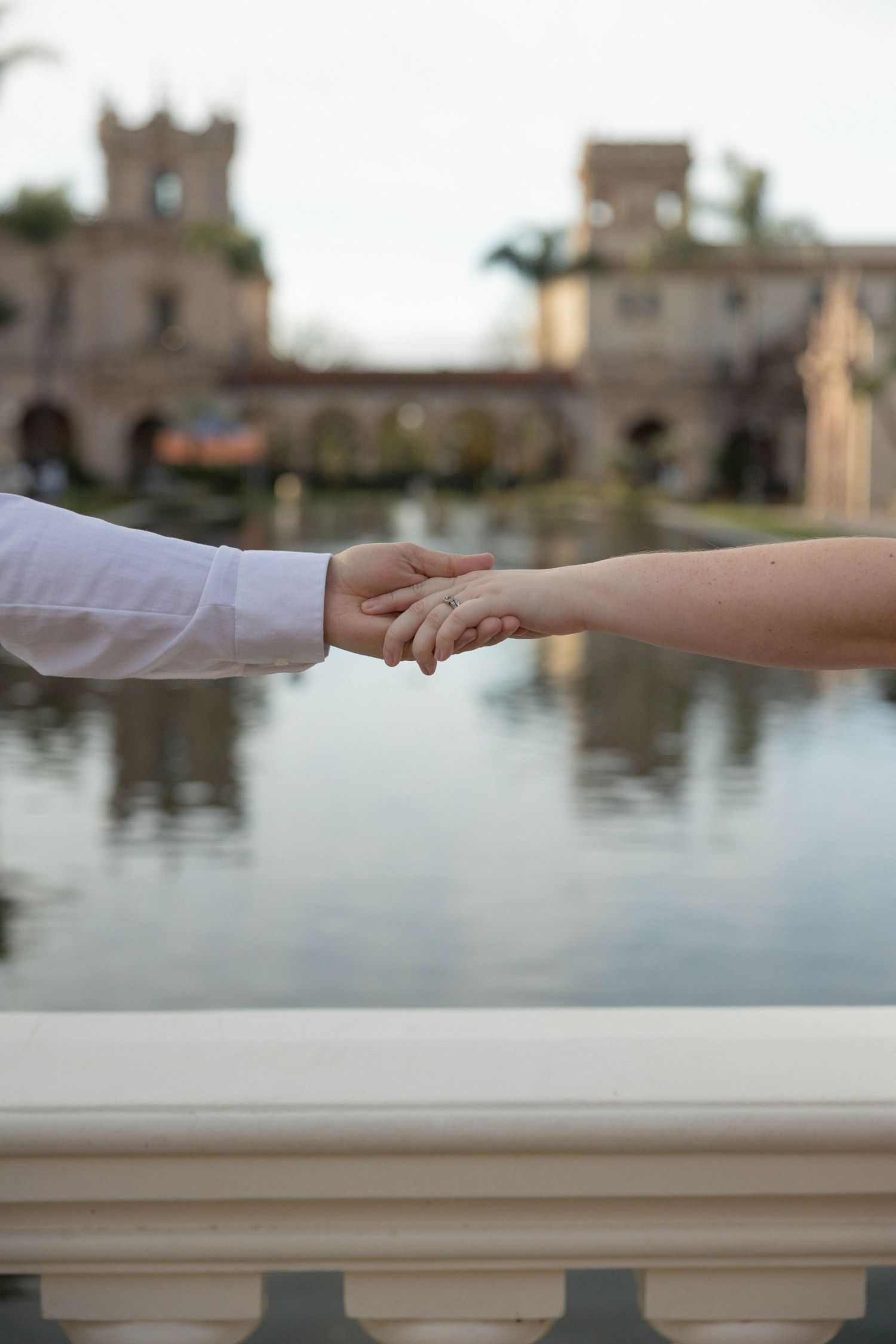 Couple holding hands near a reflective pond with a historic castle building in the background. Couples Portraits San Diego California.