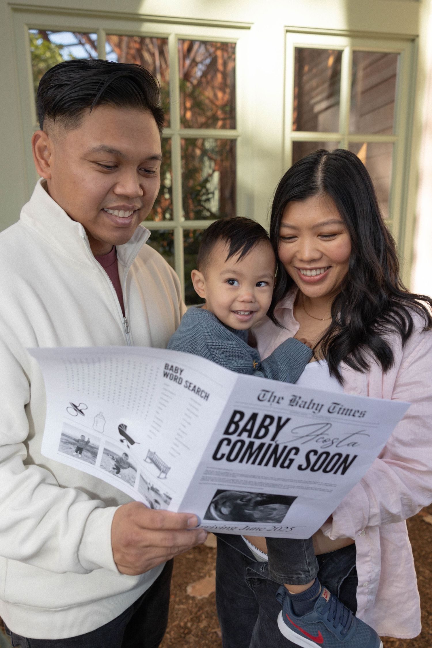 Happy family reads Baby Times newspaper announcing pregnancy, with toddler son. Maternity Photographer.