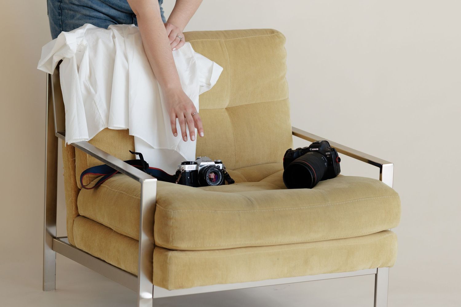 Person reaching over and placing film cameras on a vintage yellow velvet armchair with chrome frame.