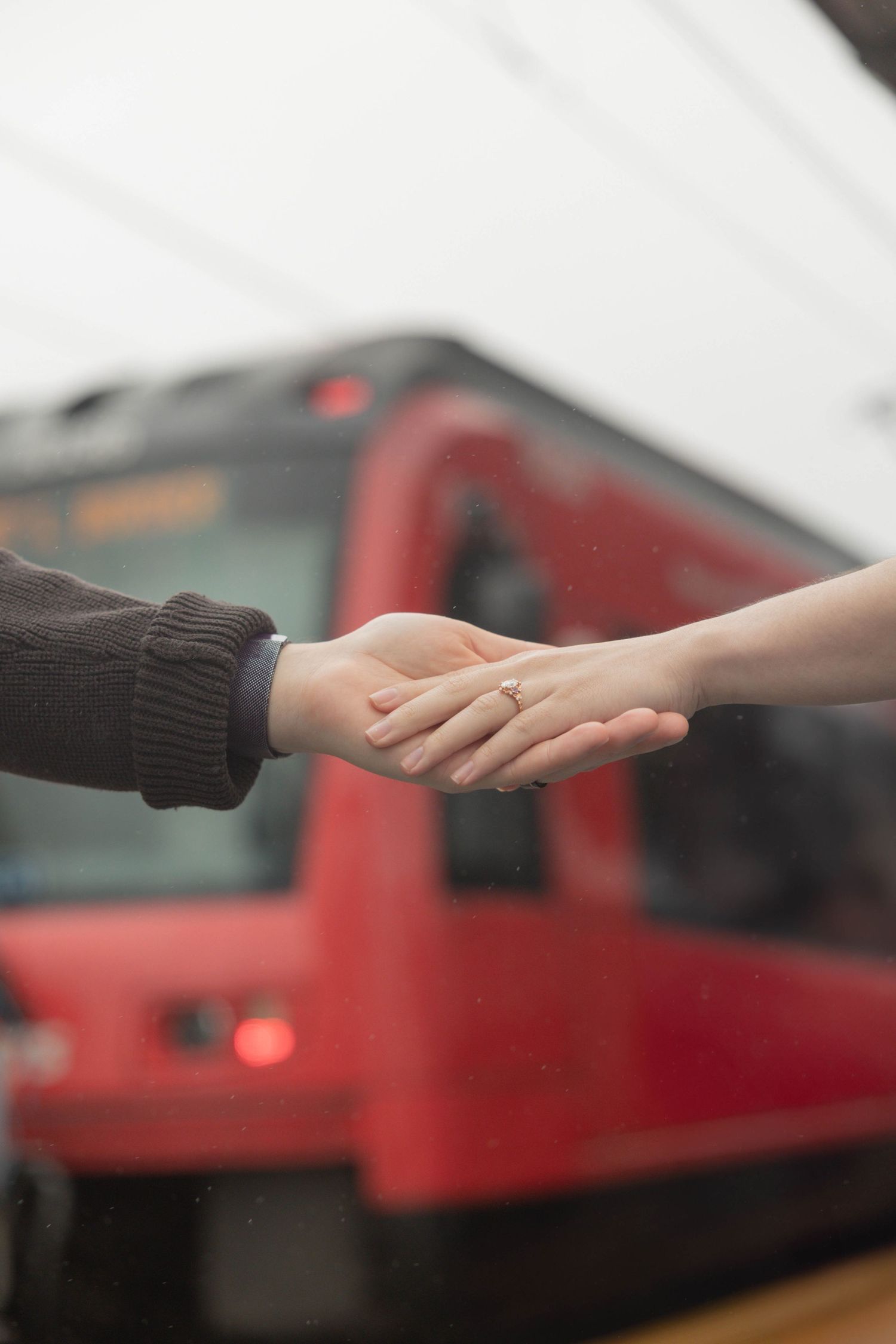 Close-up of couple holding hands with an engagement ring visible, red trolley blurred in background.