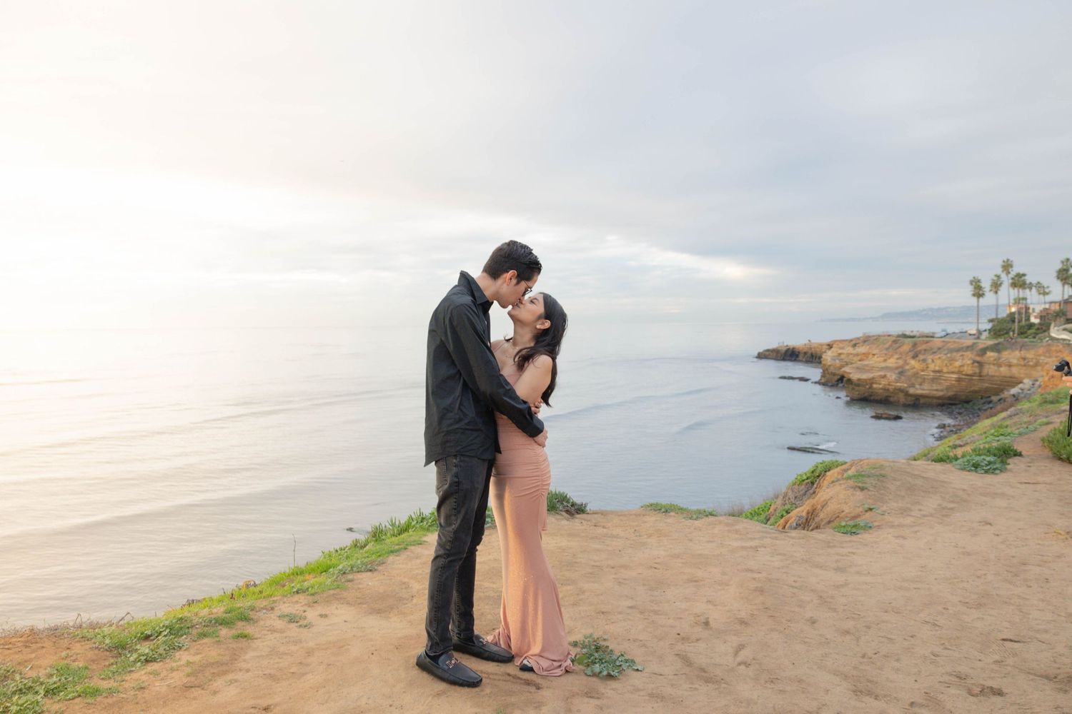 Romantic couple kissing on scenic coastal cliff at golden hour by the ocean.