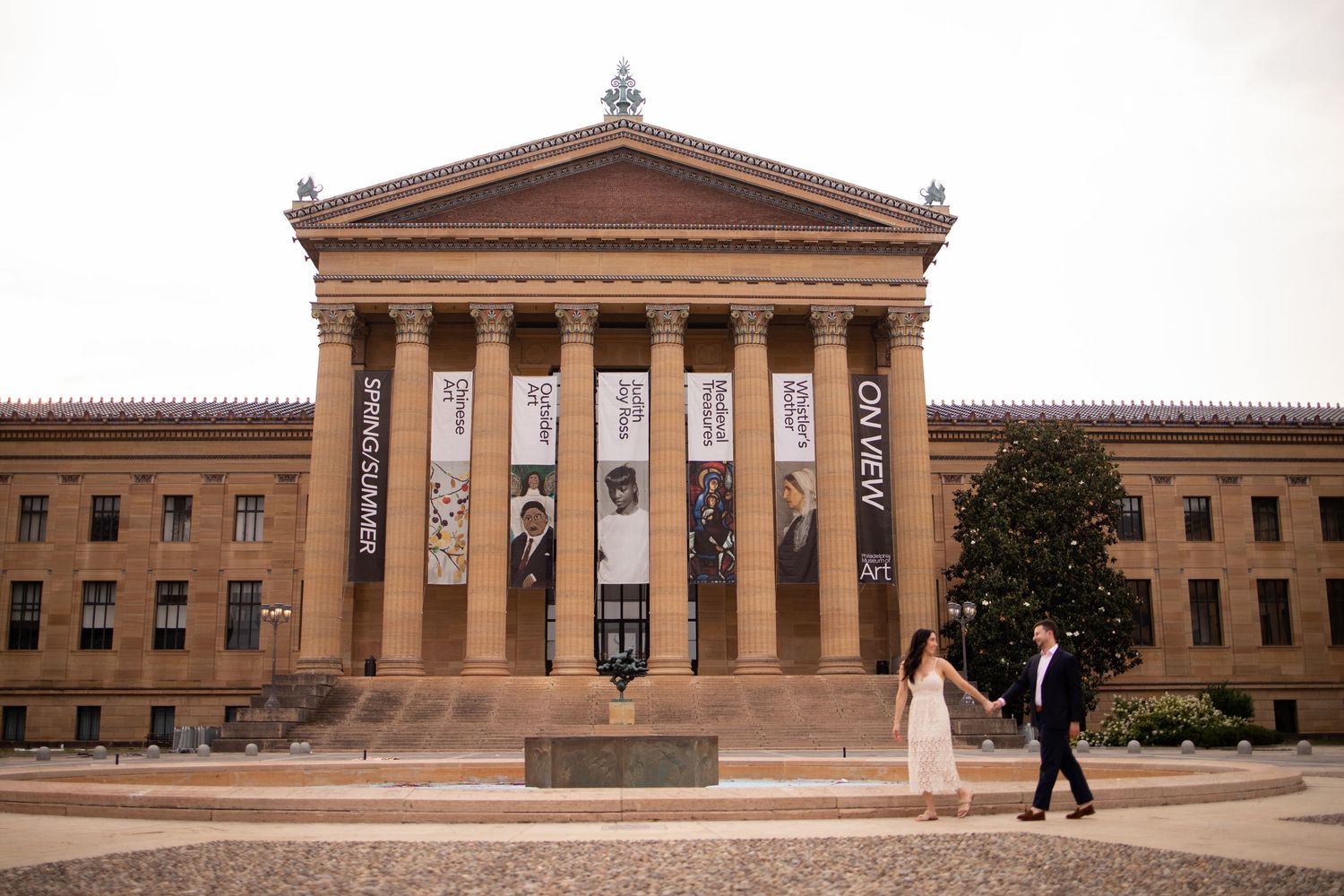 A couple walks past the grand entrance of the Philadelphia Museum of Art with its iconic neoclassical columns and facade.